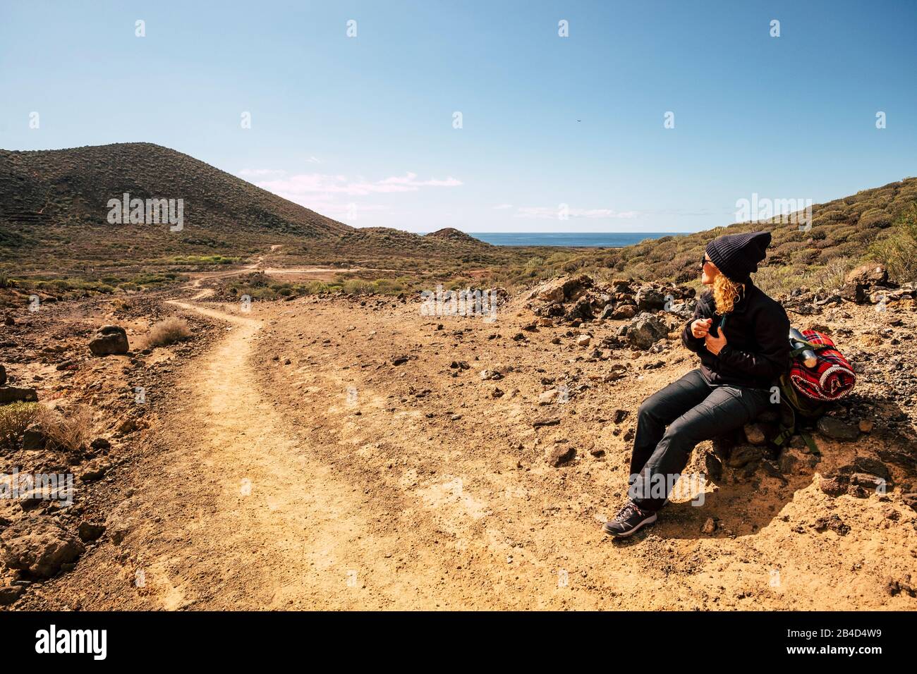 Donna attiva sedersi sulle rocce riposando durante un'attività di trekking in montagna - oceano e cielo in background, luogo panoramico per persone sano stile di vita Foto Stock