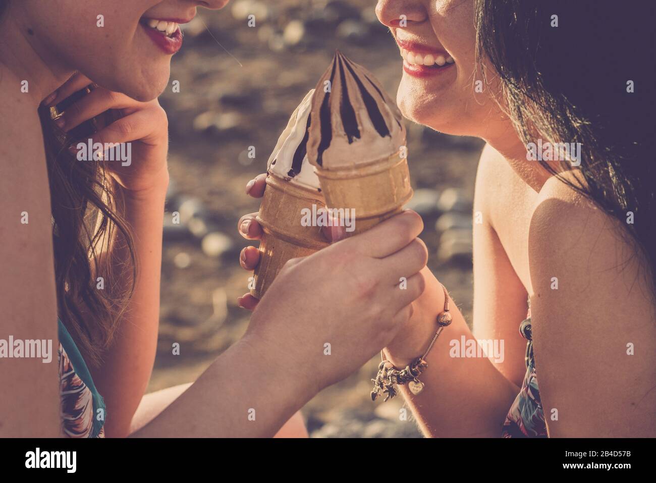 Concetto di stile estivo con coppia di allegre belle donne giovani mangiare gelato insieme in amicizia - primo piano di ragazze sorriso e lifestyle amichevole - defocused sfondo Foto Stock