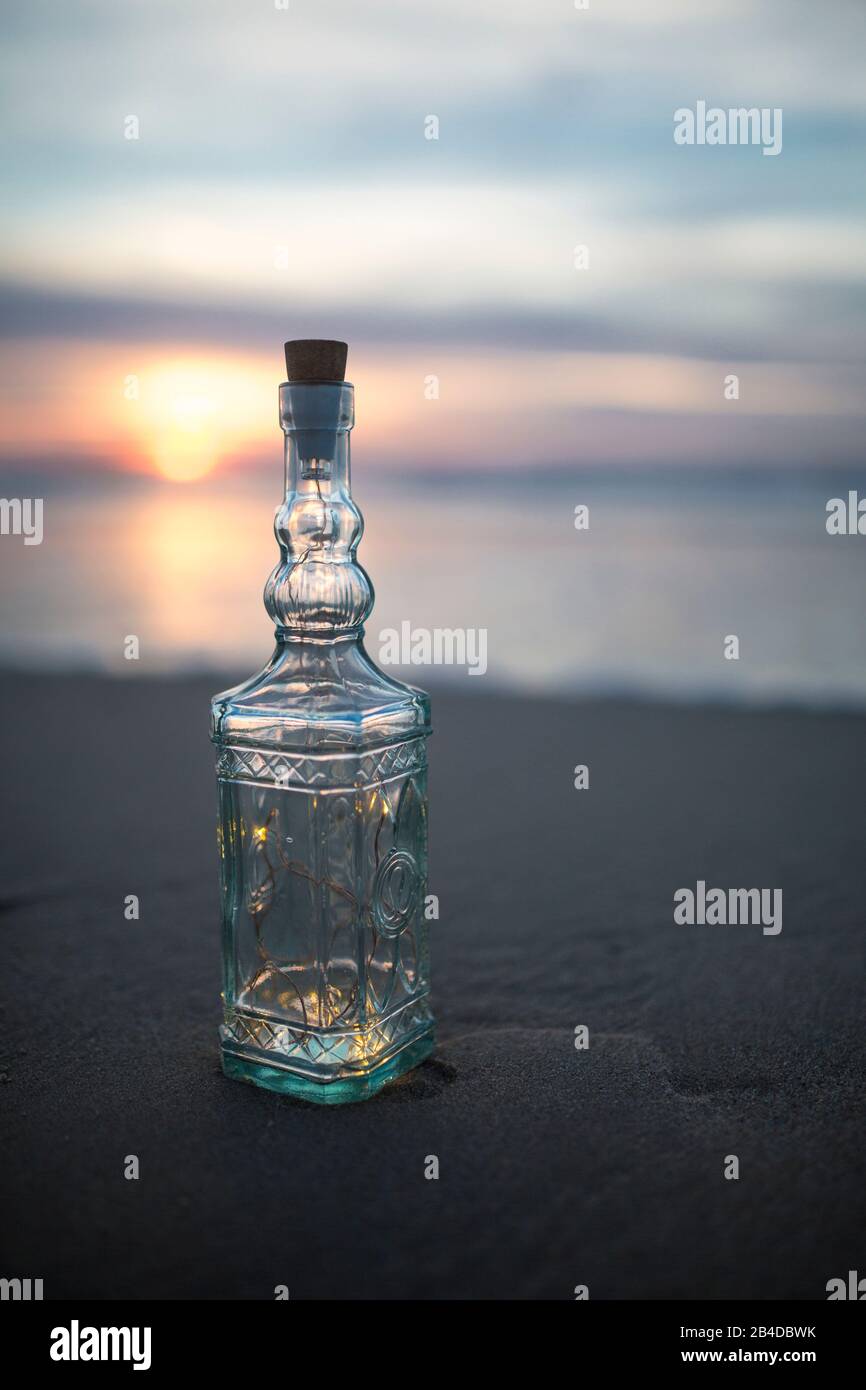 Bottiglia di vetro con decorazioni sulla spiaggia alla luce della sera Foto Stock