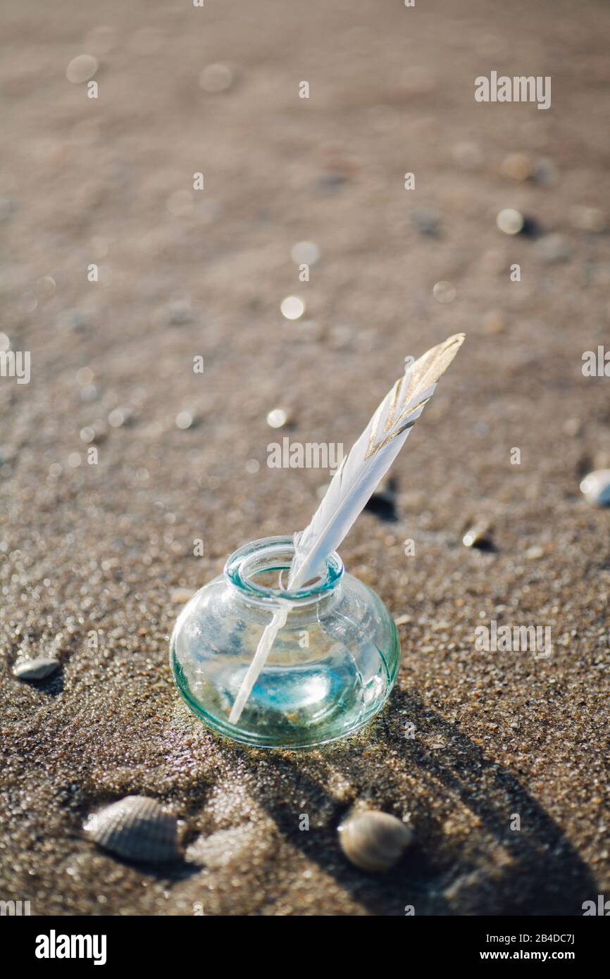 Piuma con motivo in un bicchiere sulla spiaggia Foto Stock