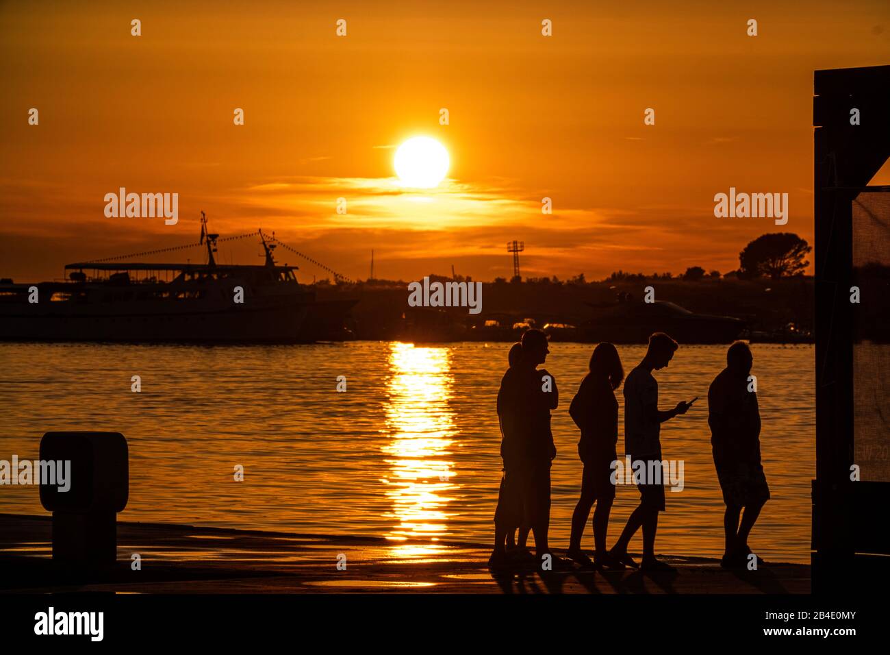 Silhouette di persone al tramonto con cielo rosso-arancione sul mare. Foto Stock