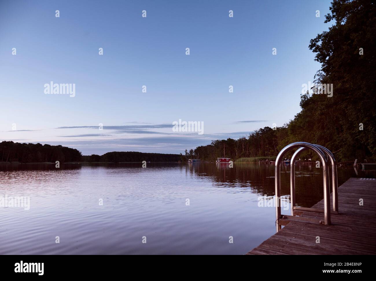 Atmosfera tranquilla e estiva su un lago della Germania dell'Est. Houseboats sono sulla riva. In primo piano un molo con scaletta da bagno Foto Stock