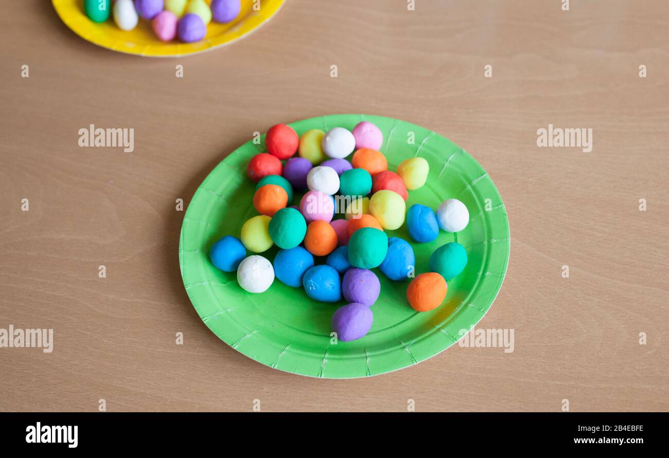Piatto di plastica pieno di palline colorate di pasta da gioco. Sfondo in legno Foto Stock