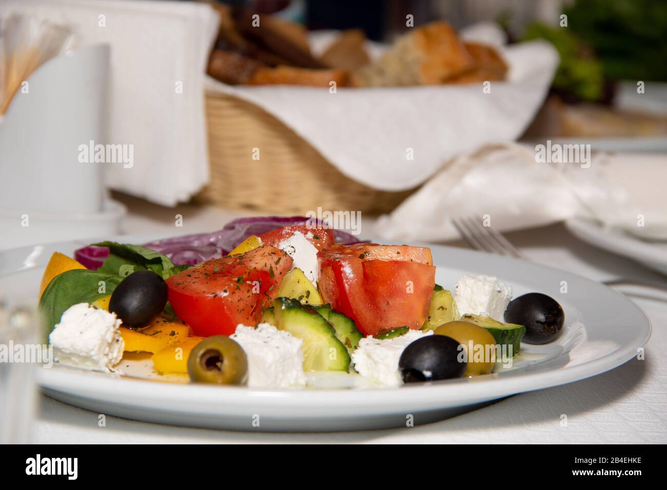 Insalata greca con peperone dolce fresco, cipolla rossa, pomodori ciliegini arancioni, cetrioli, olive nere e feta conditi olio extra vergine di oliva su woode Foto Stock