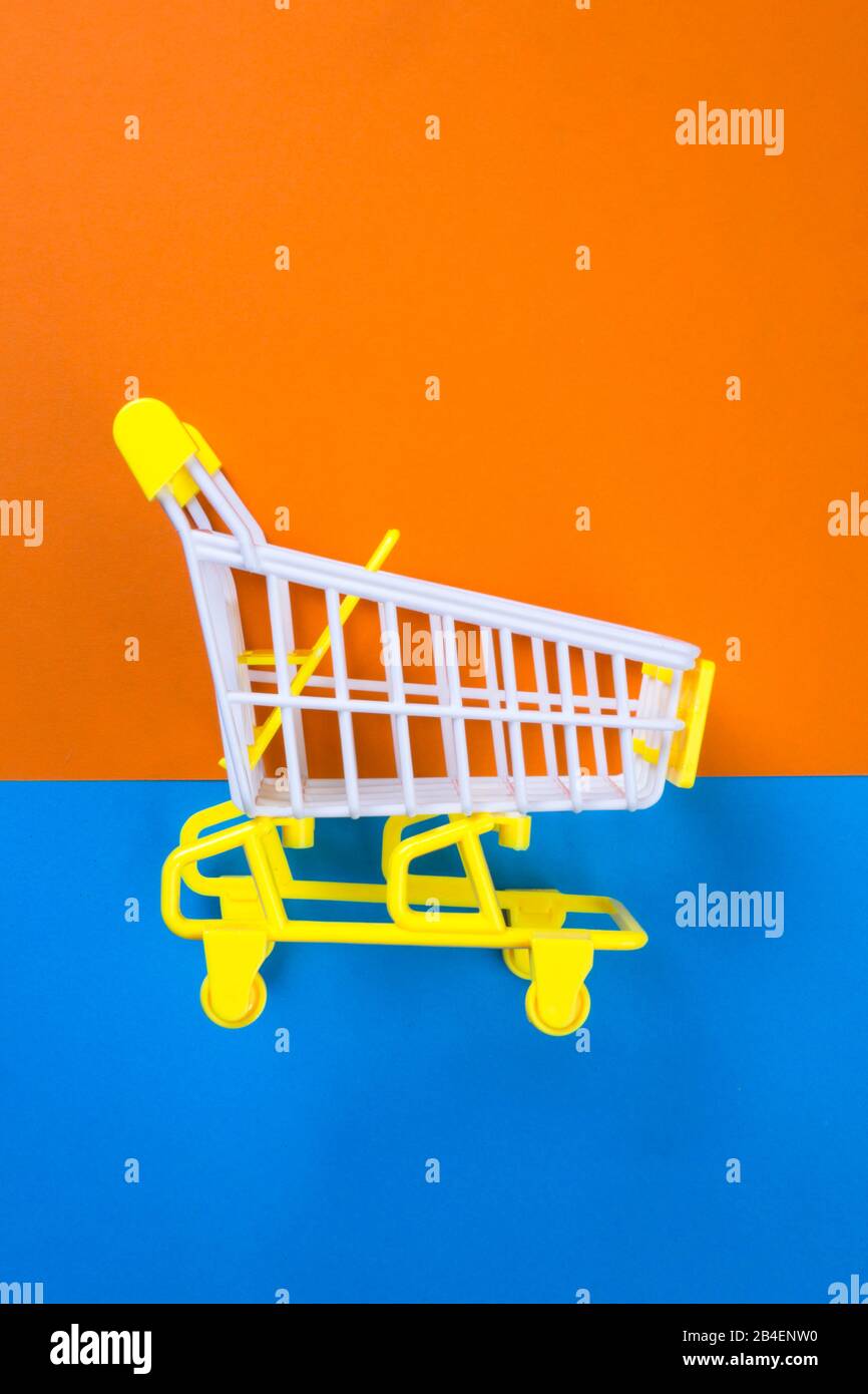 Shopping piccolo trolley su sfondo arancione e blu, Copy space. Vendita o acquisto di concetto di consumatore Foto Stock