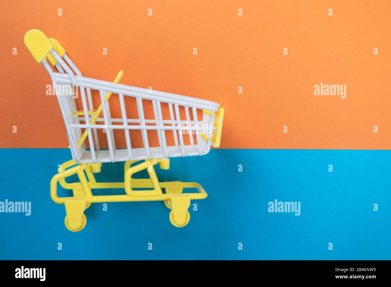 Shopping piccolo trolley su sfondo arancione e blu, Copy space. Vendita o acquisto di concetto di consumatore Foto Stock