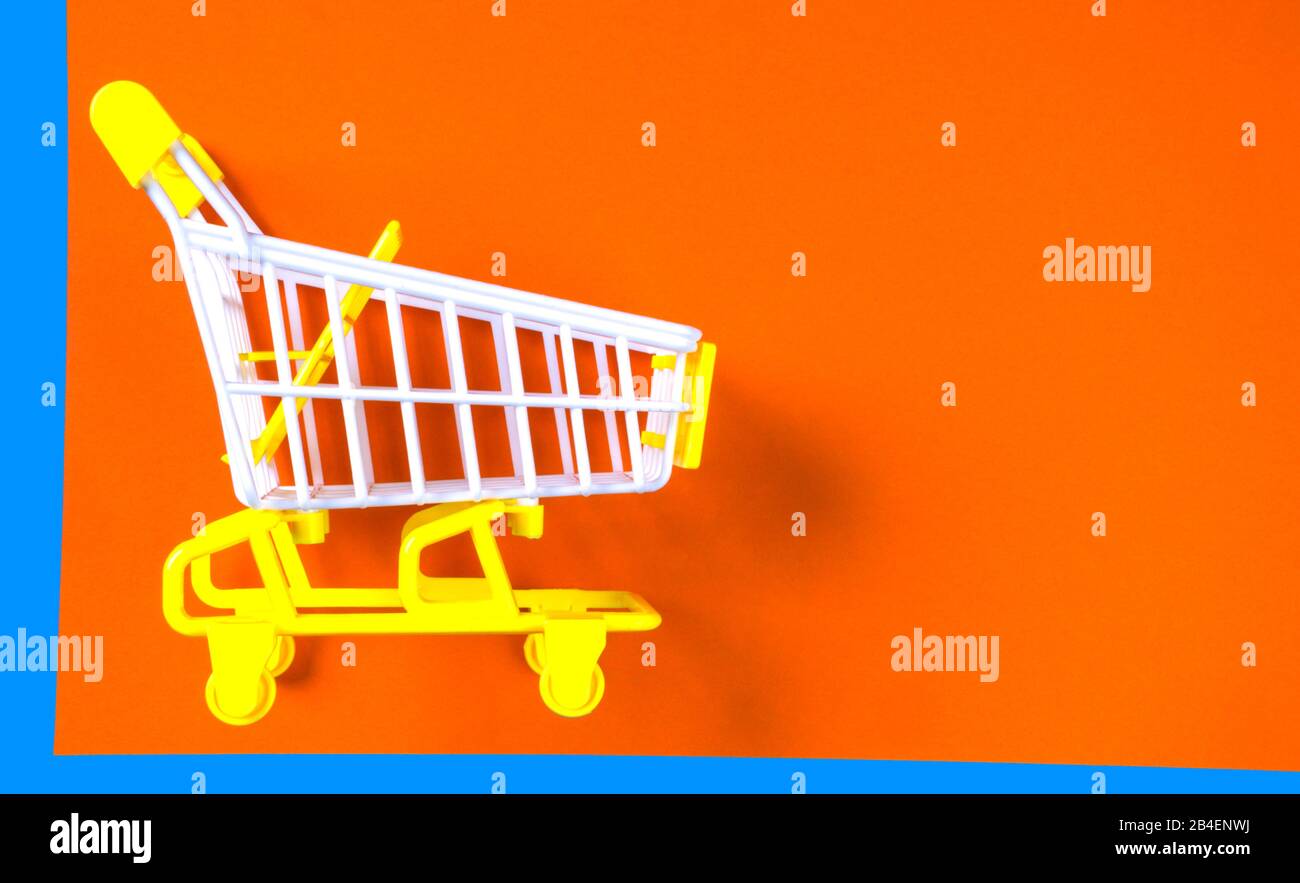 Shopping piccolo trolley su sfondo arancione e blu, Copy space. Vendita o acquisto di concetto di consumatore Foto Stock