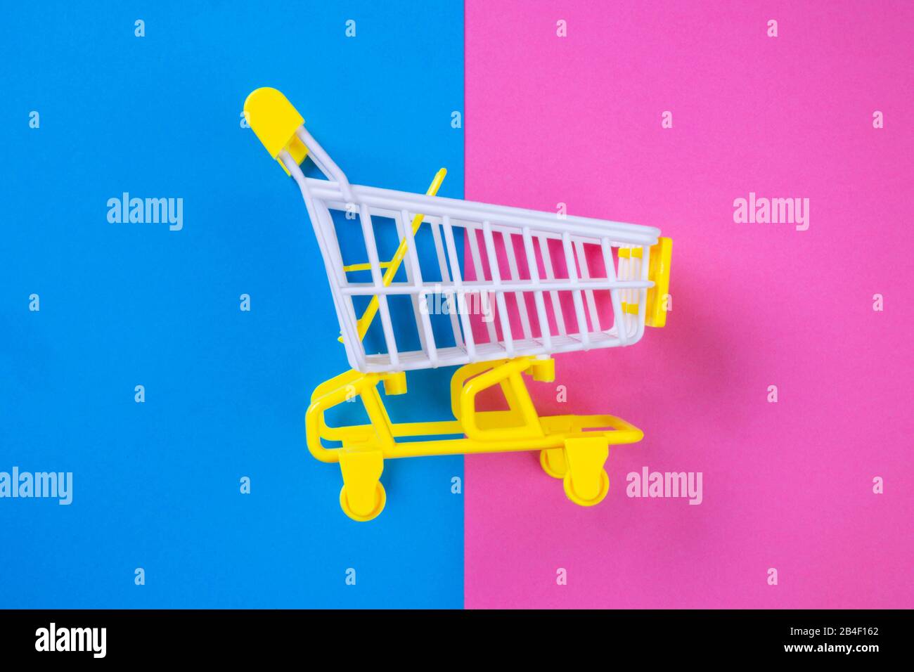 Shopping piccolo trolley su sfondo blu e rosa, Copy space. Vendita o acquisto di concetto di consumatore Foto Stock
