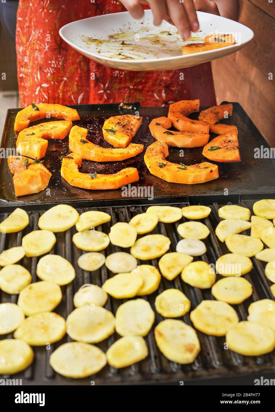 Pezzi di zucca con butternut arancione posizionati sulla superficie della griglia elettrica dalla piastra bianca, taglio della patata sfocato ai cerchi in primo piano. Foto Stock