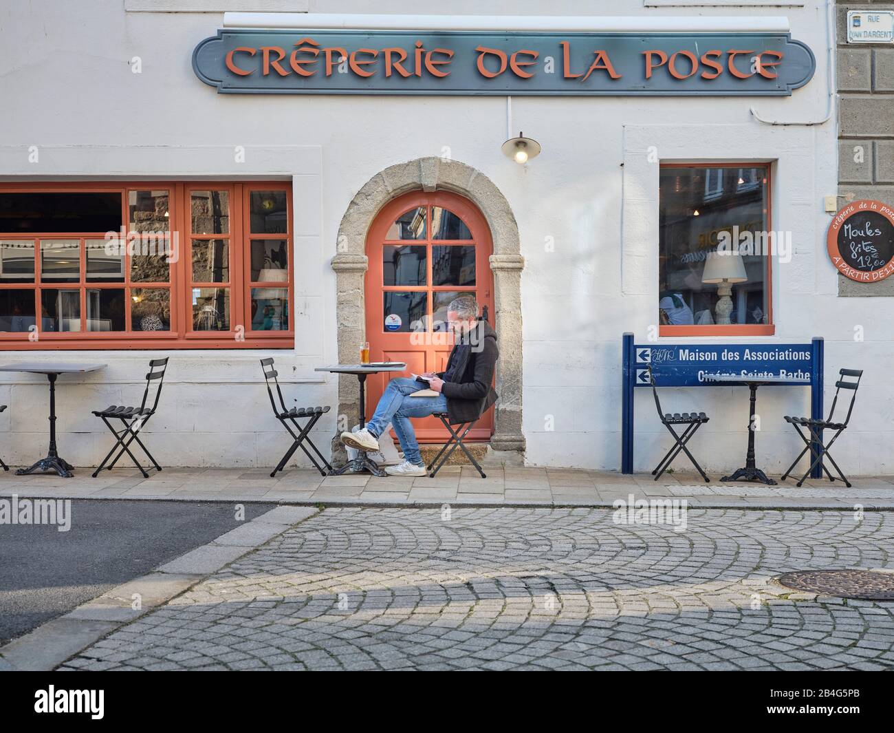 Ein Man ließt ein Buch vor einer Crêperie a Roscoff in der Bretagne. Foto Stock