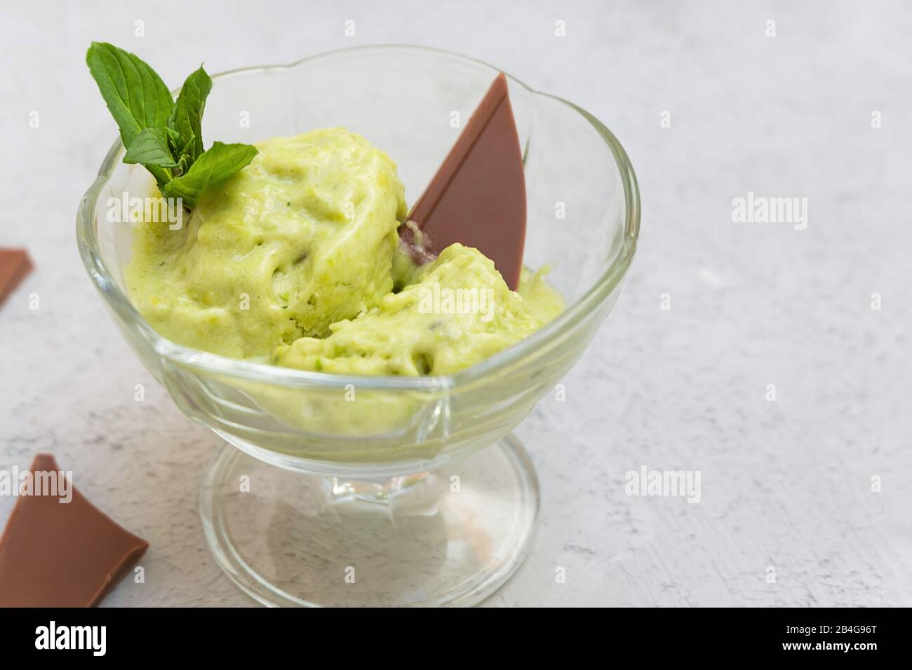 Immagine ravvicinata di un sano gelato avocado in una ciotola di vetro su fondo neutro di cemento Foto Stock