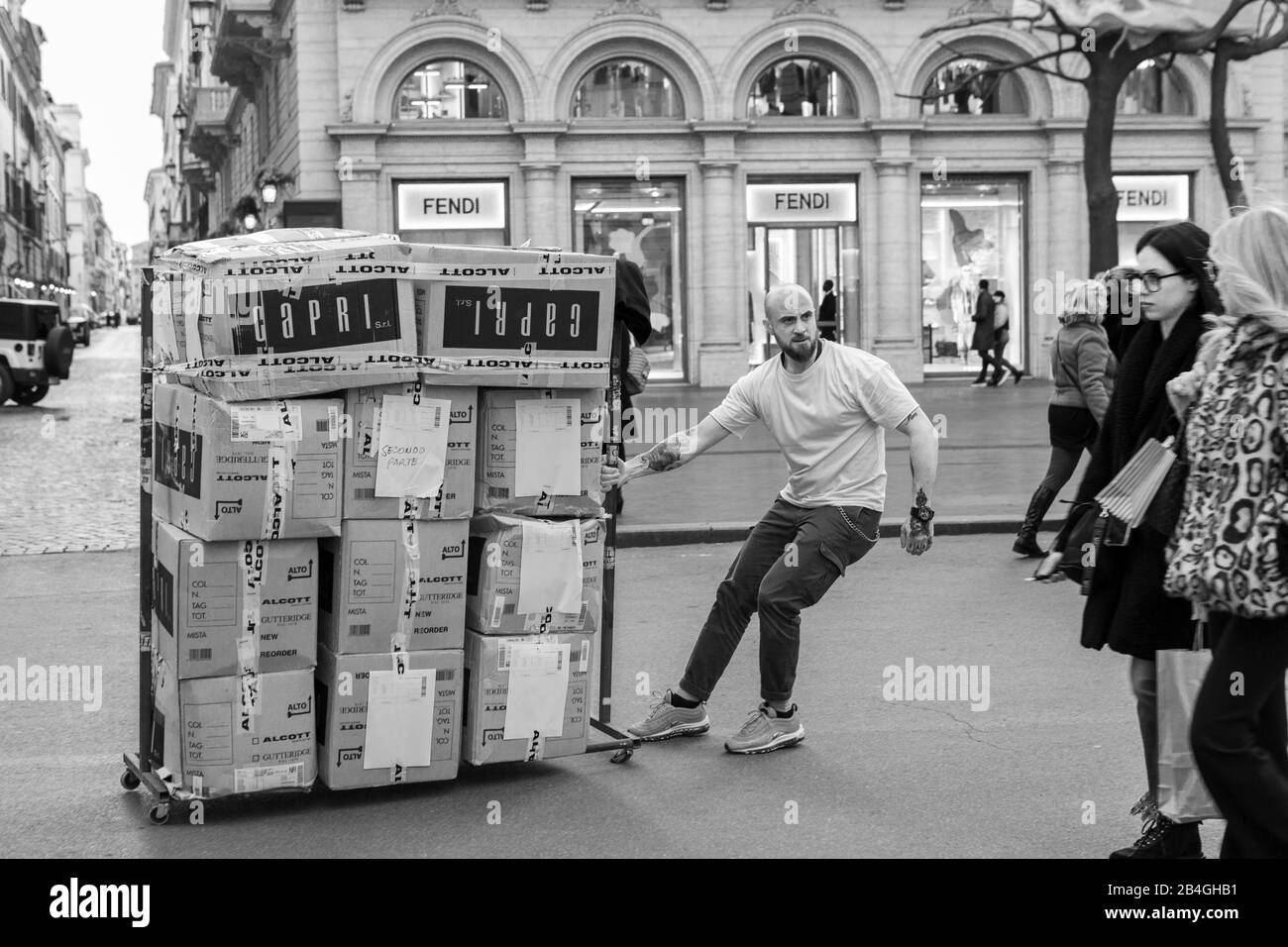 Uomo che trascina un pallet contenente scatole di articoli di abbigliamento di fronte al negozio Fendi a Roma, Italia Foto Stock