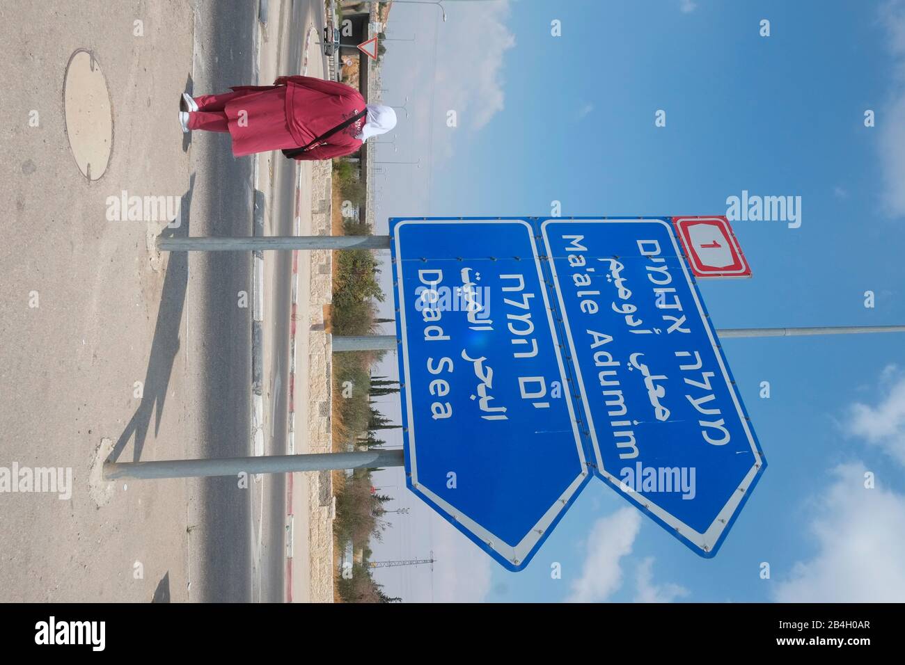 Donna musulmana che si trova accanto al segno bilingue di destinazione Foto Stock