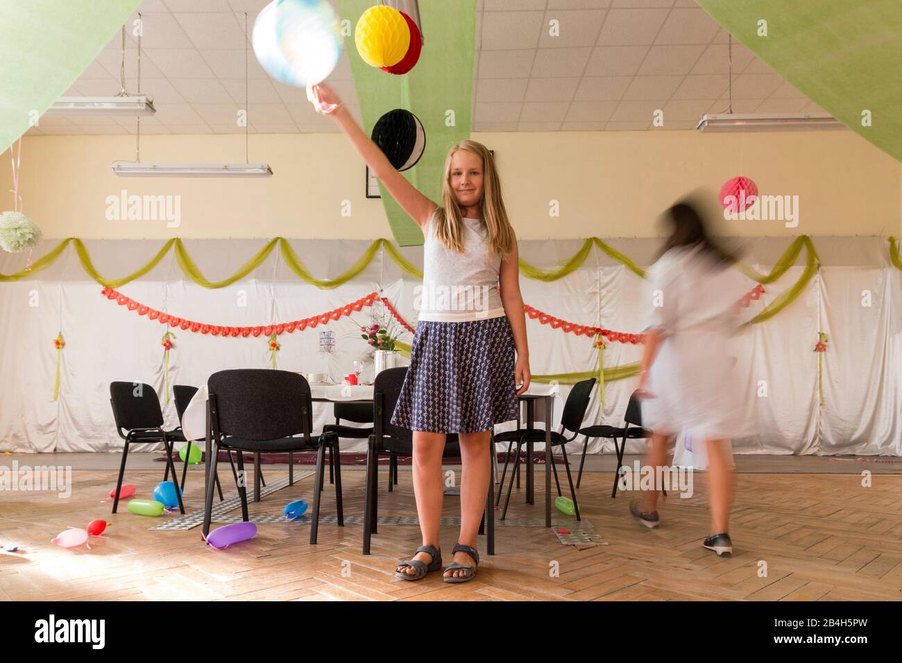 Una ragazza tiene un palloncino in aria mentre gli ospiti di altre parti si puliscono o sono già andati, Foto Stock