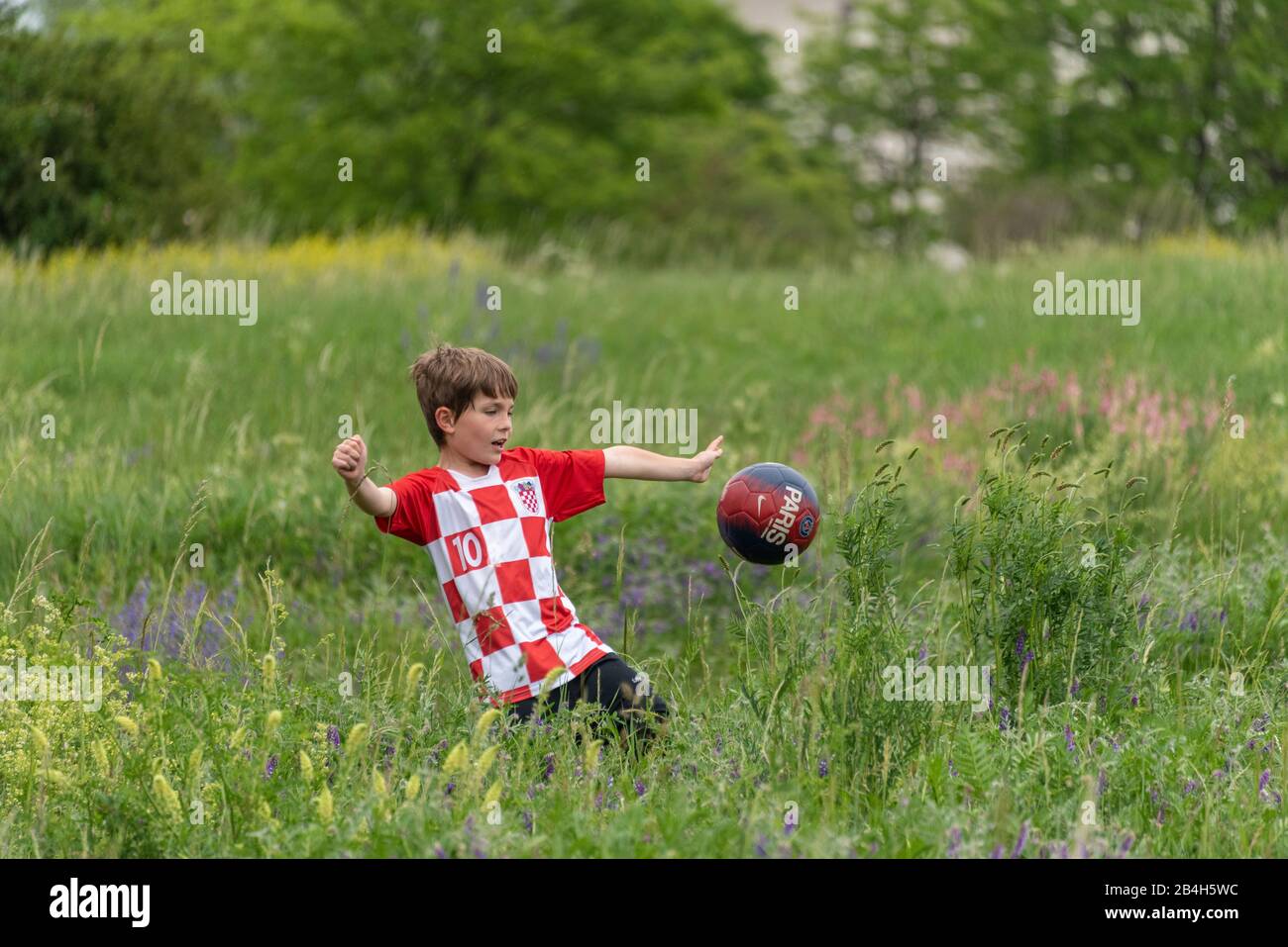Un ragazzino con maglia croata gioca a calcio nell'erba alta, Foto Stock