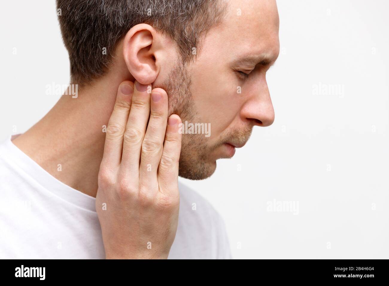 Primo piano ritratto di malato tocca le ghiandole linfatiche con le dita vicino all'orecchio, sofferente di dolore, occhi chiusi, isolato. Linfadenite, immun Foto Stock