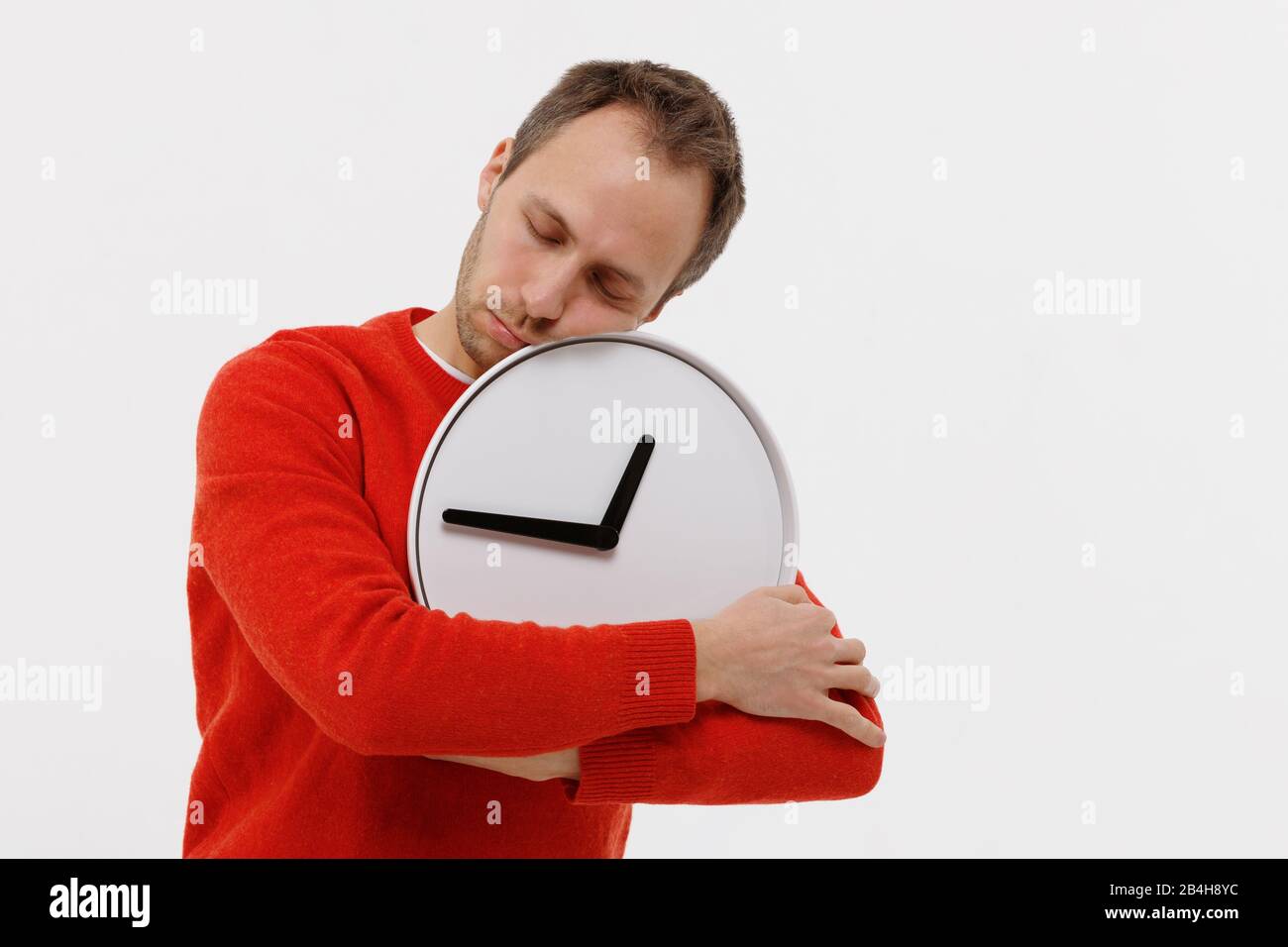 Studio ritratto di uomo stanco si è addormentato con un orologio rotondo, tenendo le mani, isolato su sfondo bianco. Mancanza cronica di sonno, insonnia, phys Foto Stock