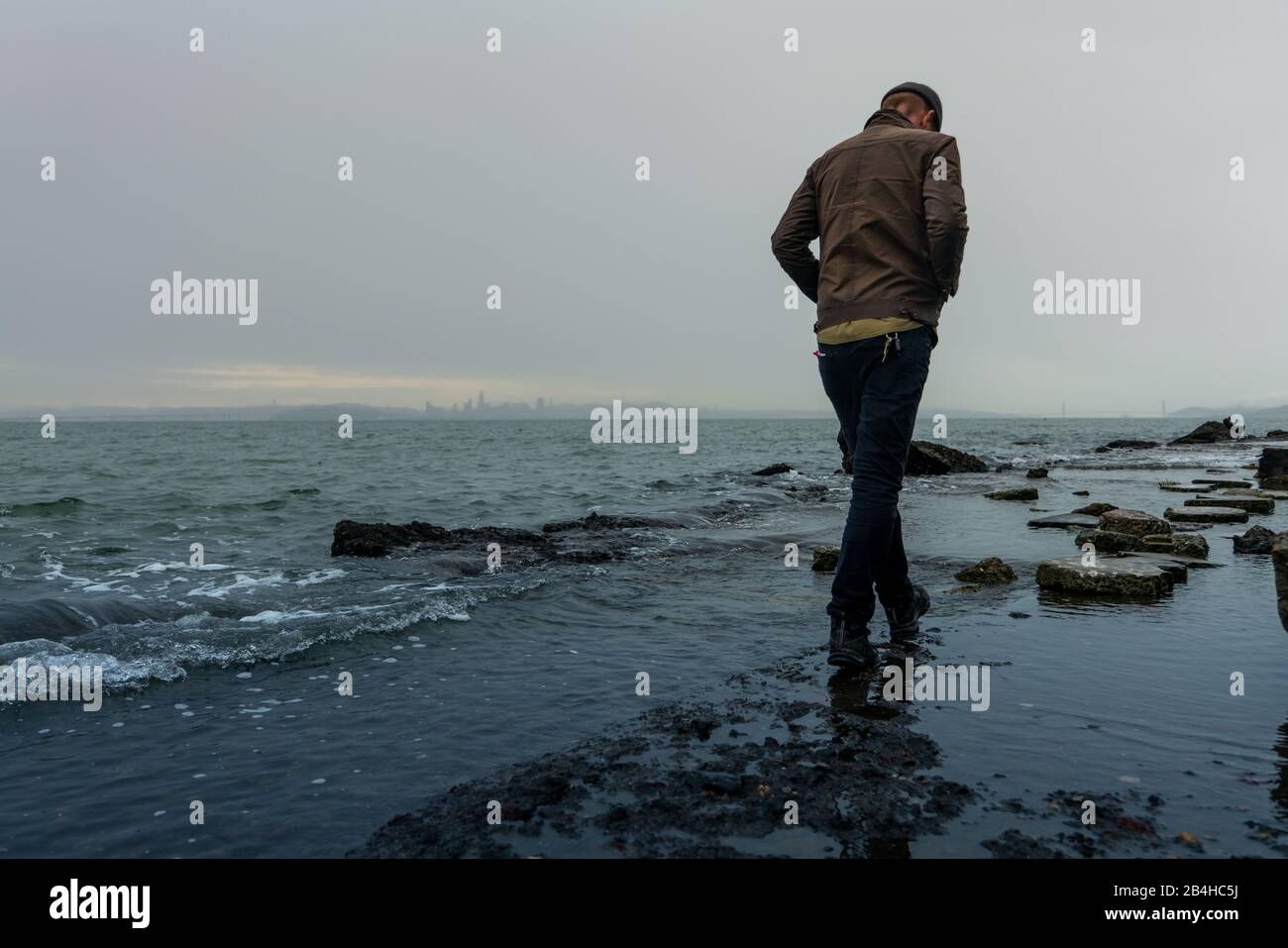 L'uomo fa un sentiero che attraversa bayside con la silhouette della città all'orizzonte Foto Stock