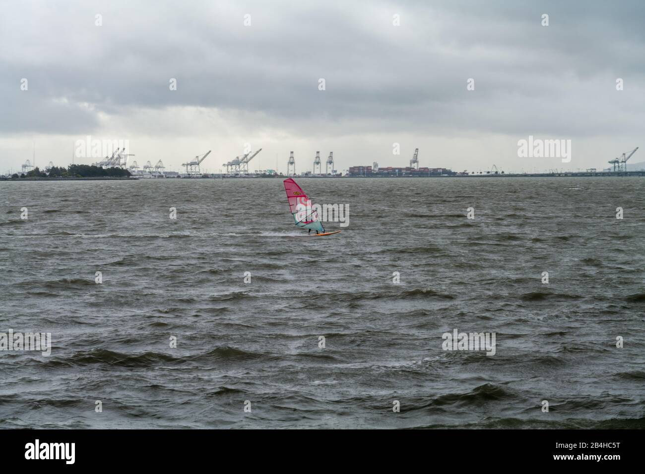 Windsurf che naviga attraverso la baia con gru da trasporto in background Foto Stock