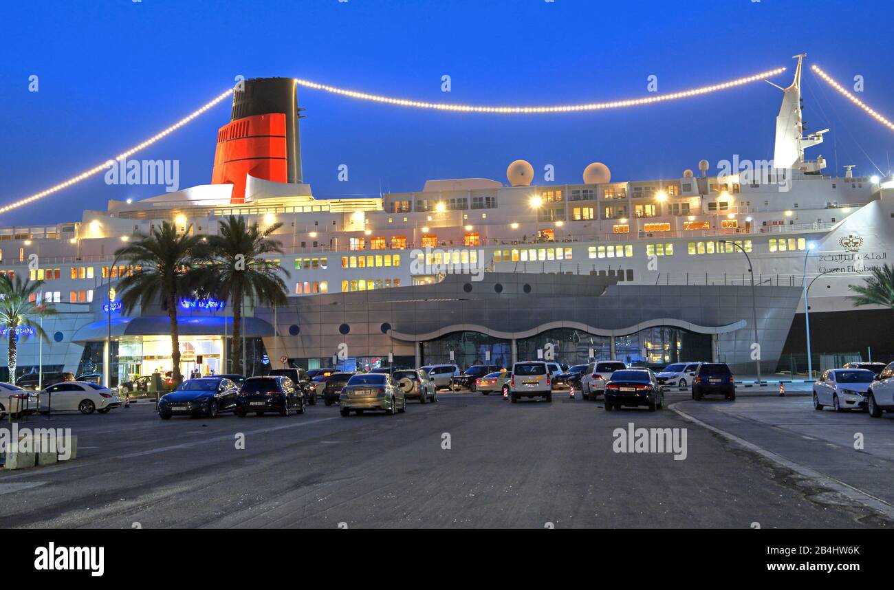 Hotel illuminato e nave museo Regina Elisabetta 2 (QE2) al molo al tramonto, Dubai, Golfo Persico, Emirati Arabi Uniti Foto Stock