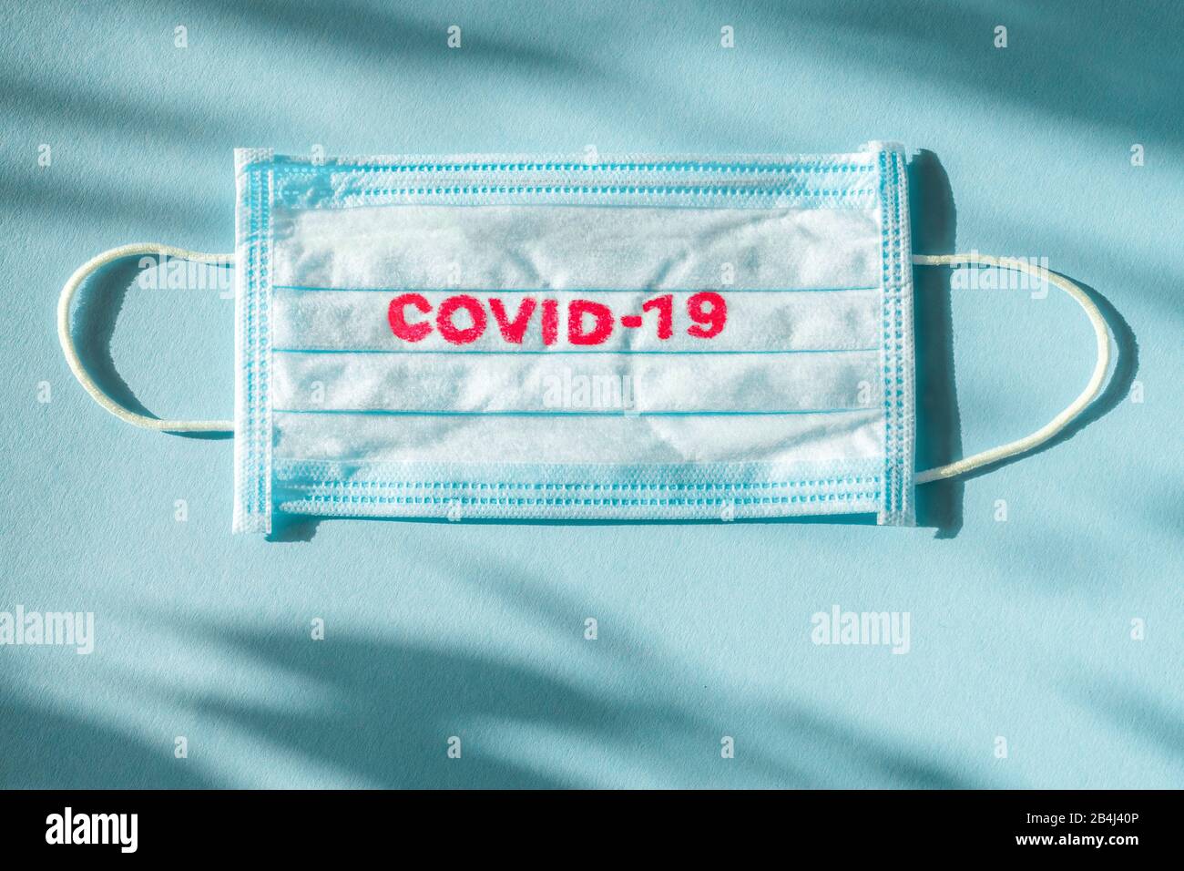 Covid-19 - Il Romanzo di Wuhan Coronavirus polmonite ottiene il nome ufficiale DA CHI: COVID-19. Medicazione monouso sul viso. Contesto sanitario. Maschera facciale monouso per uso medico blu con stampa covid-19 Foto Stock