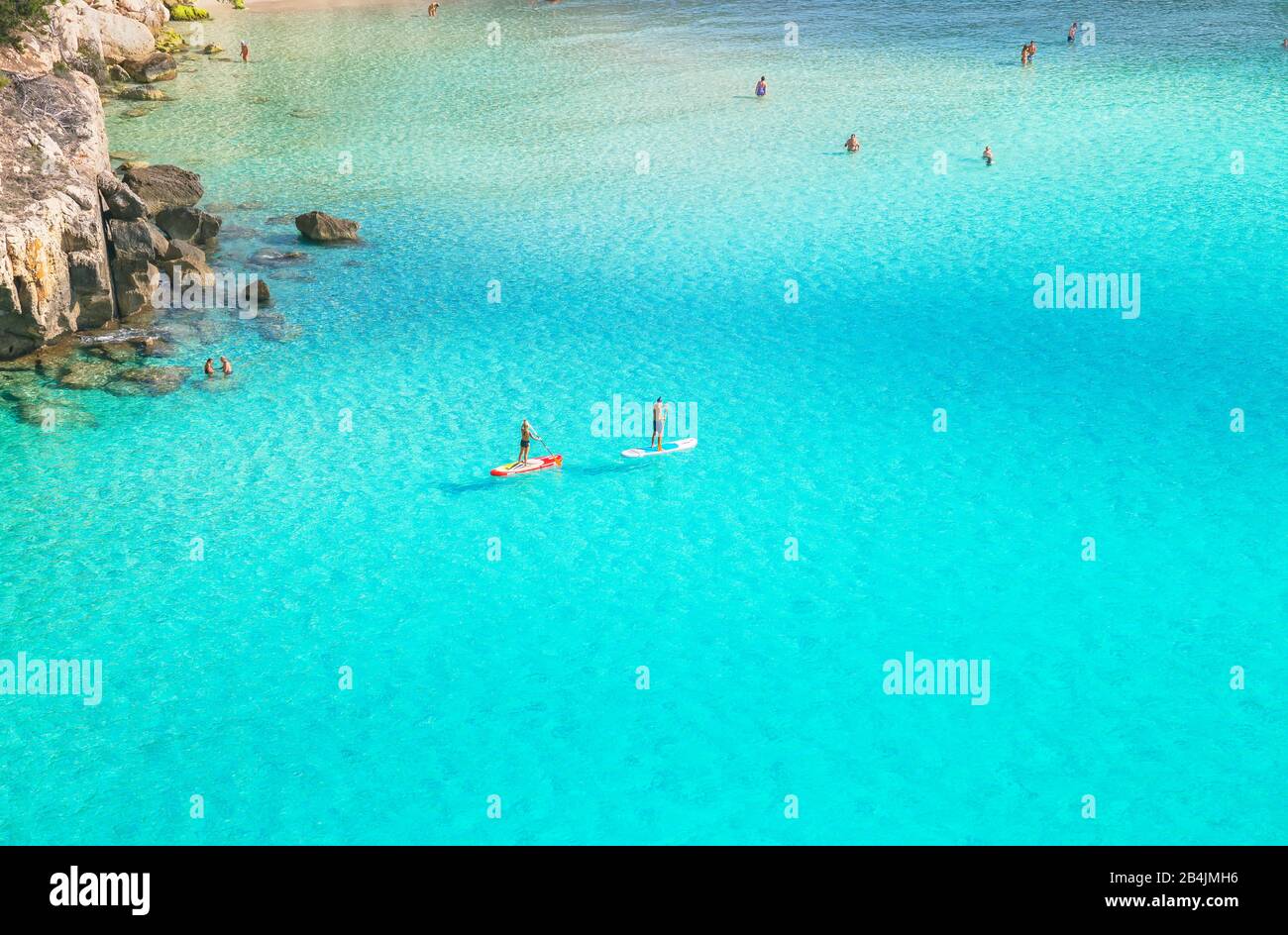 Stand-up paddler nelle acque verde smeraldo di Cala Mitjana, Minorca, Isole Baleari, Spagna, Europa Foto Stock