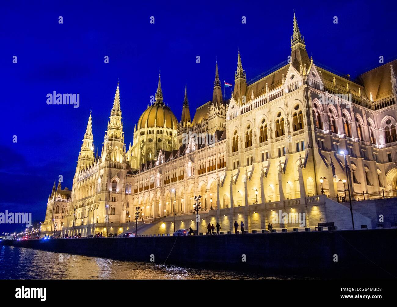 Riflessioni parlamentari: Facciata illuminata degli edifici del Parlamento ungherese dal fiume. Foto Stock