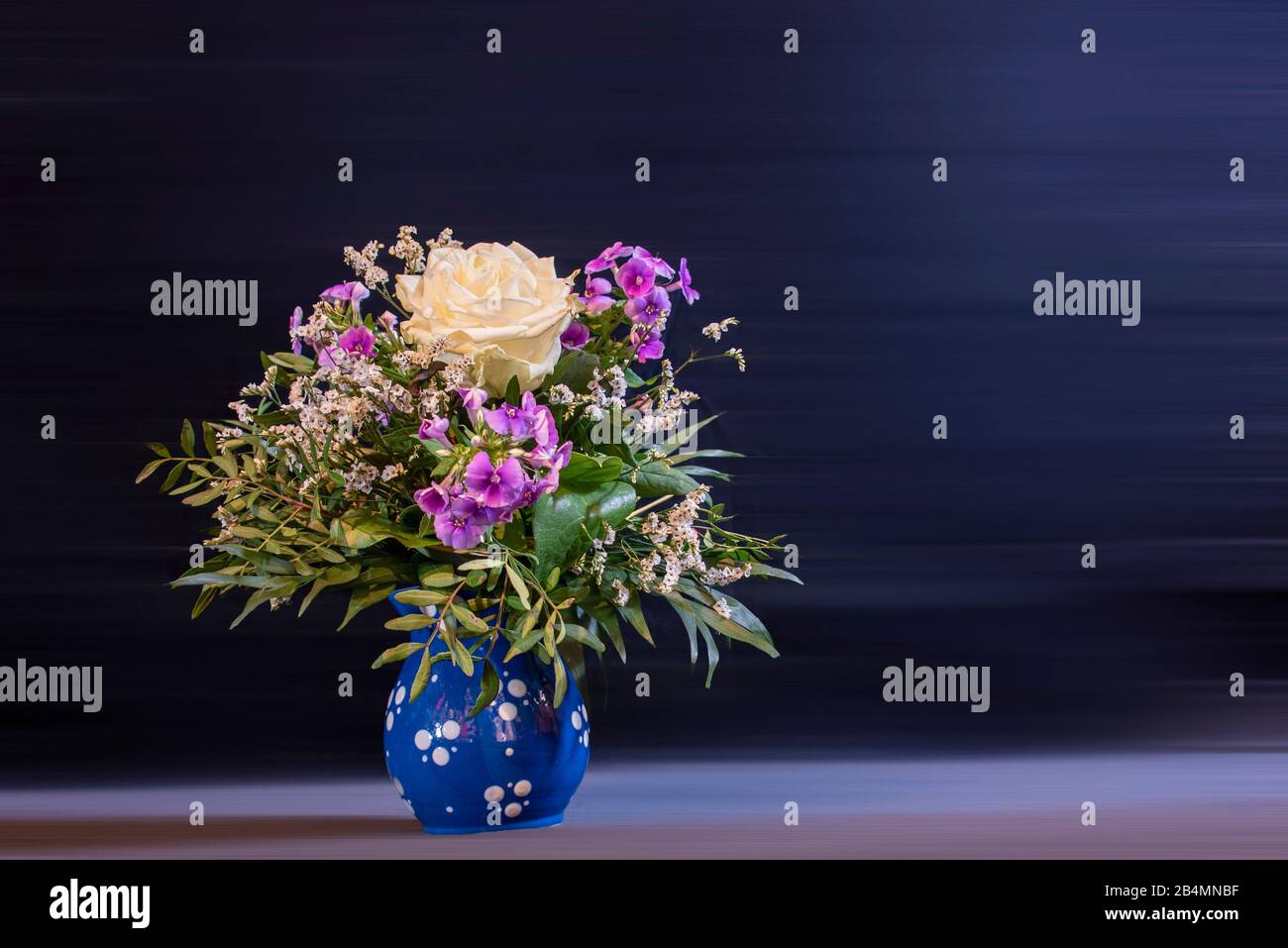 Un bouquet festoso di fiori si staglia in un vaso blu con puntini bianchi. Foto Stock