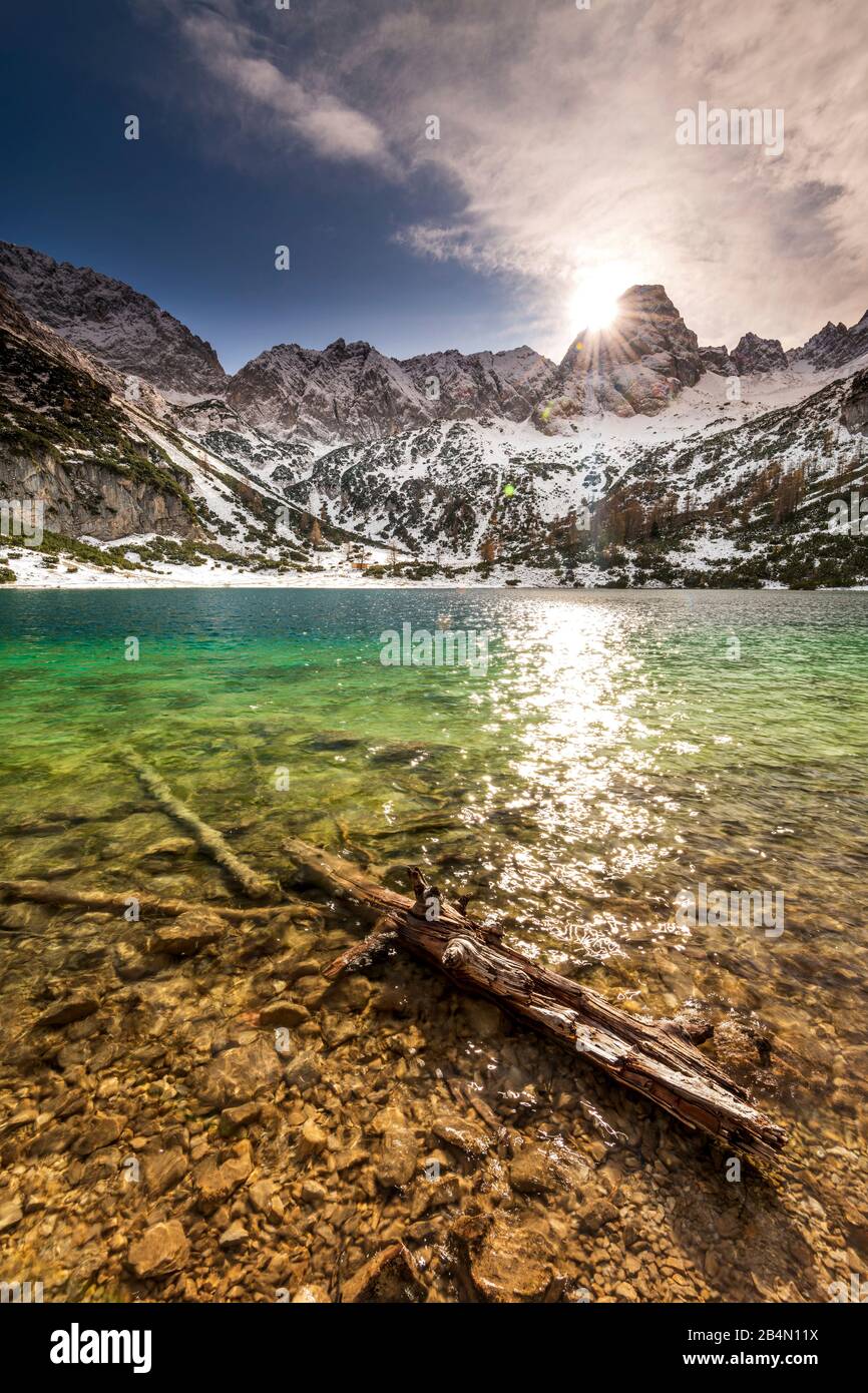 I raggi solari si riflettono nel Seebensee. Un vecchio log sulla banca punta alle acque cristalline e turchesi in inverno. Foto Stock