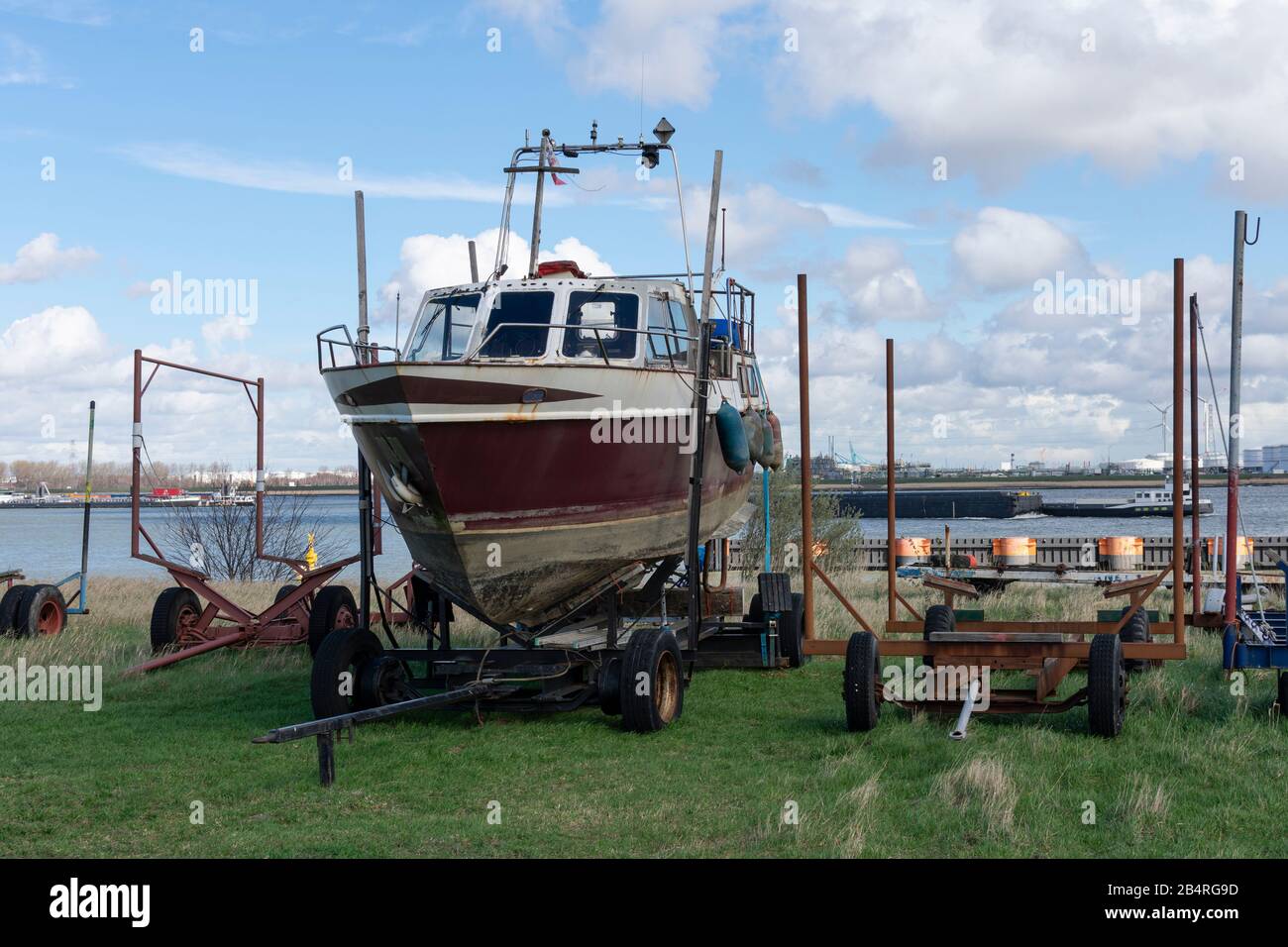 Vecchia barca in attesa sul molo su un rimorchio per il restauro, sullo sfondo il porto di Anversa Foto Stock