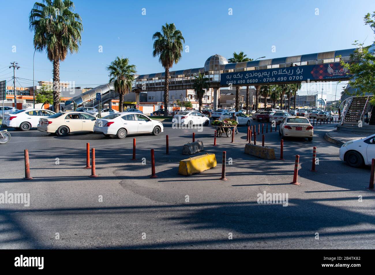 Iraq, Kurdistan iracheno, Erbil. Vista di un incrocio. Un uomo sta camminando nella direzione opposta delle automobili mentre spinge un carrello pieno di fiori Foto Stock