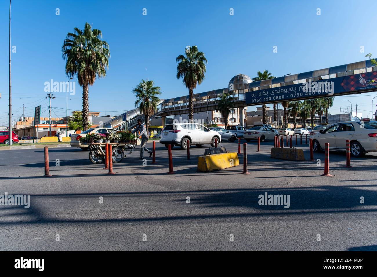 Iraq, Kurdistan iracheno, Arbil, Erbil. Vista di un incrocio. Un uomo sta camminando nella direzione opposta delle automobili mentre spinge un carrello pieno di galleggianti Foto Stock
