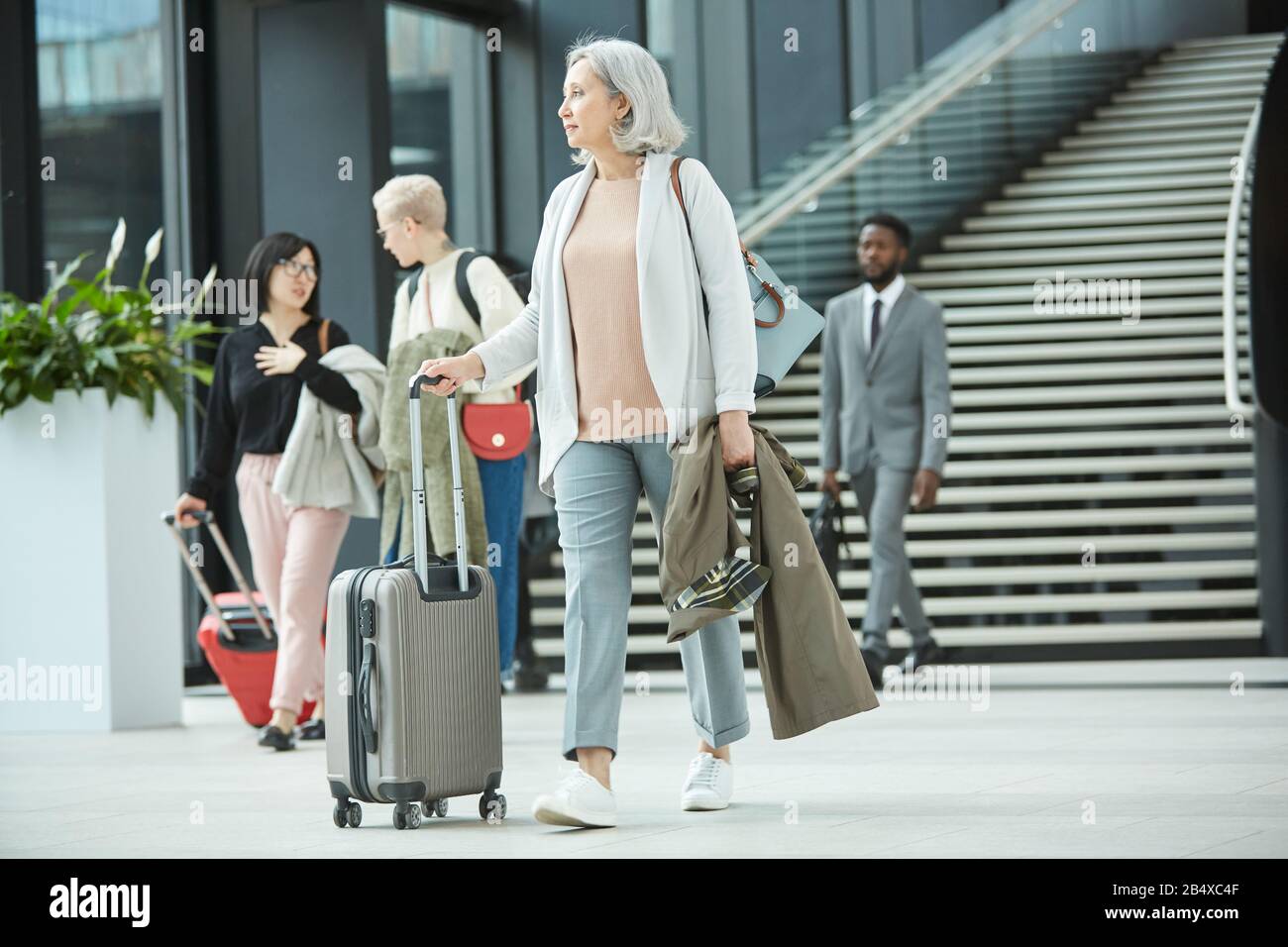 Full shot orizzontale di donna moderna senior che cammina lungo la sala dell'aeroporto con i suoi bagagli, copia spazi Foto Stock