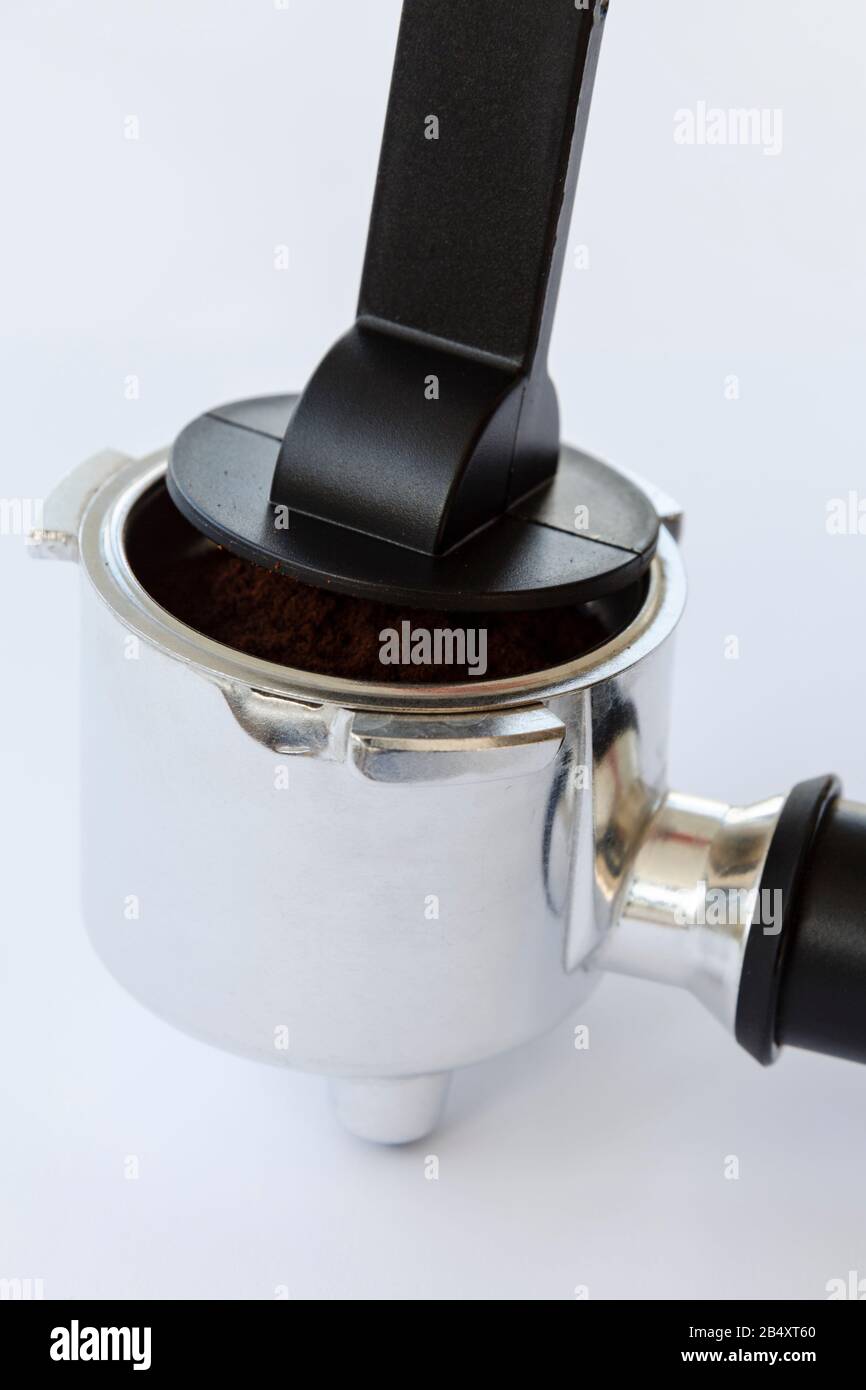 Pressatura del caffè macinato in una macchina da caffè domestica portafiltro portafiltro con manomissione in plastica su fondo liscio Foto Stock