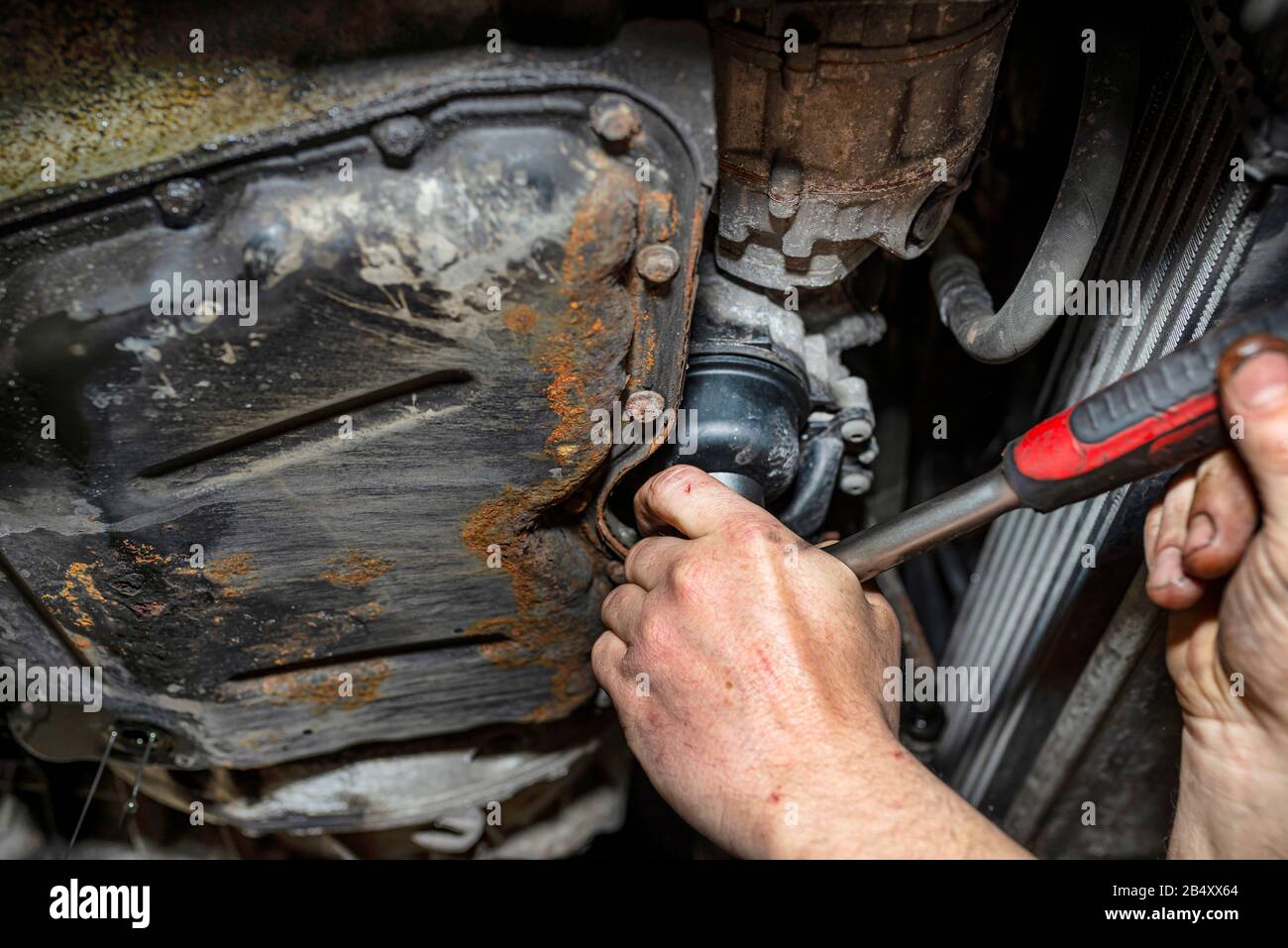 Il meccanico del veicolo sviti il filtro diesel accanto alla coppa dell'olio con una chiave metallica, mani uomo visibili. Foto Stock