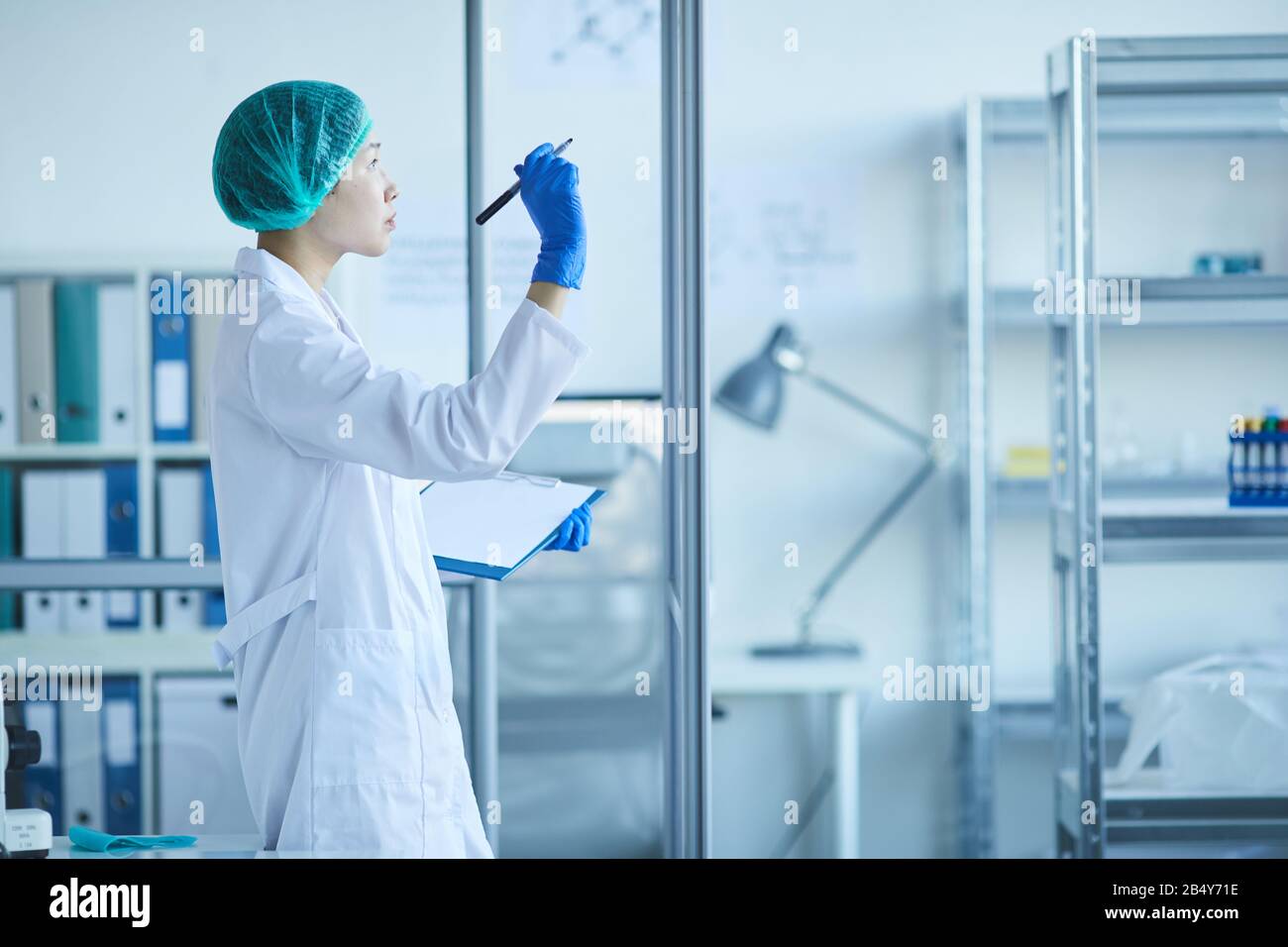 Orizzontale medio lungo lato colpo di vista della donna asiatica laboratorio scienziato scrittura formule su parete di vetro Foto Stock