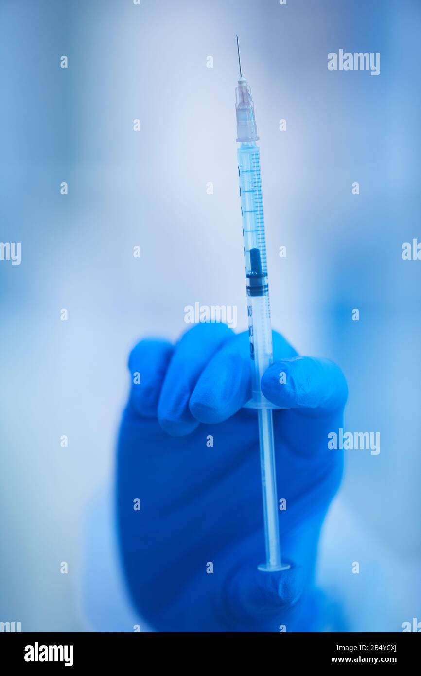 Mano della donna in una siringa blu usa e getta in lattice per il mantenimento del glive piena di nuovo vaccino, colpo ravvicinato verticale Foto Stock