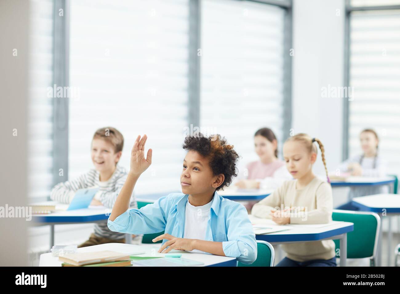 Ritratto orizzontale di Smart African American scuola media studente alzando la mano per dare risposta in classe, copia spazio Foto Stock