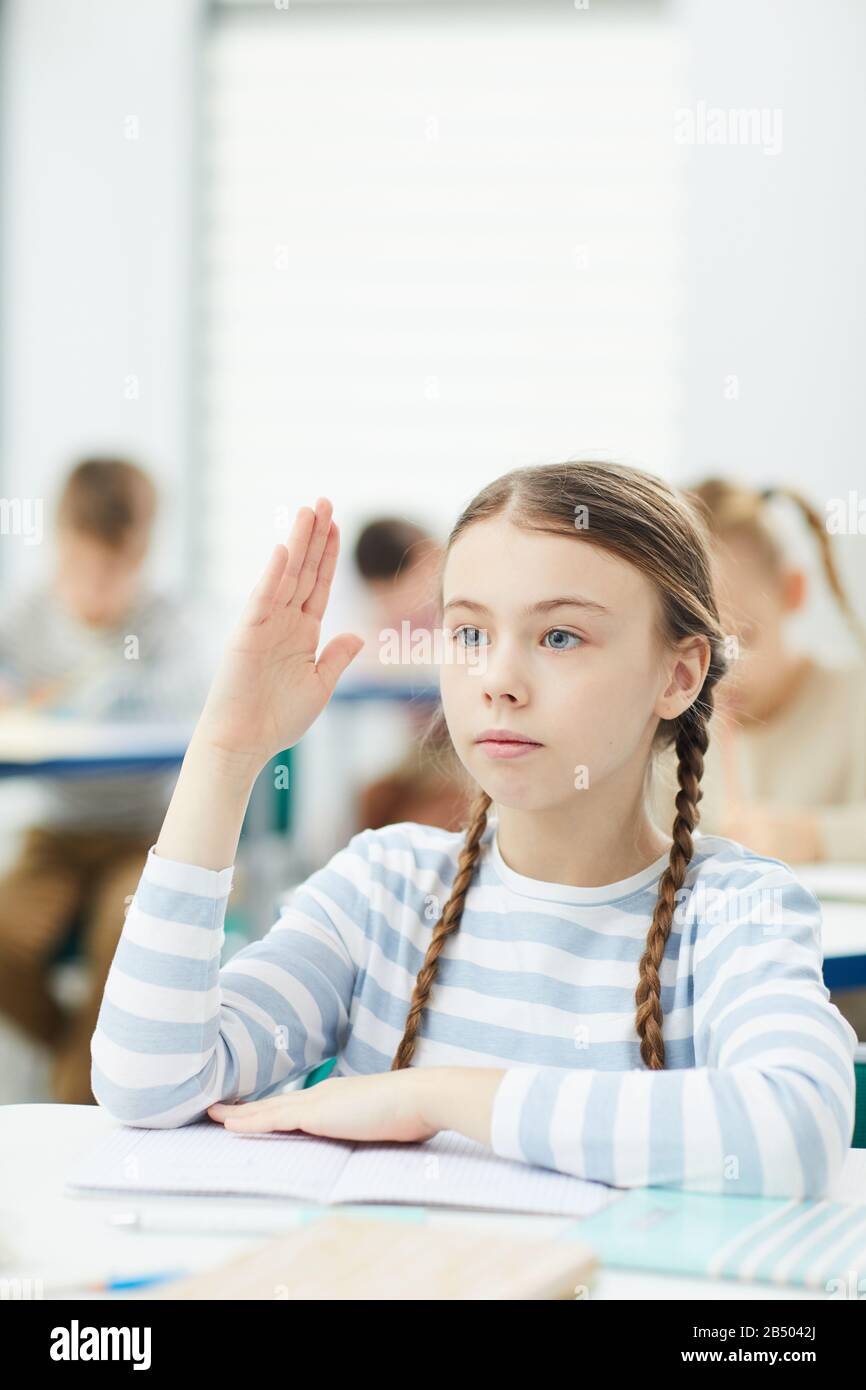 Il ritratto verticale della scuola elementare intelligente onora lo studente seduto alla scrivania della scuola alzando la mano in classe, copiare lo spazio Foto Stock
