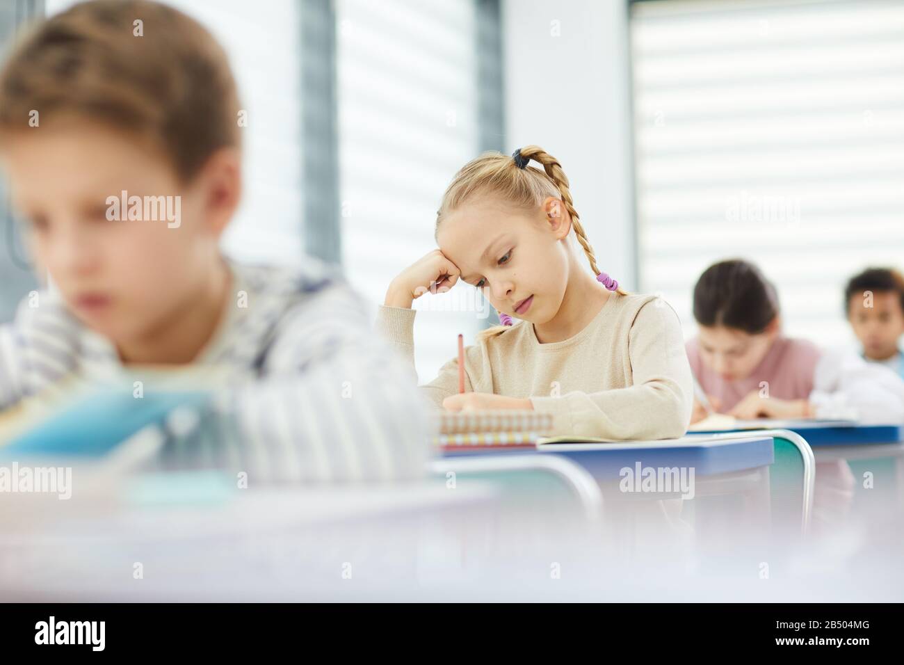 Ritratto orizzontale scatto di ragazza caucasica pensiva con capelli biondi composizione scritta durante la lezione di tempo, copia spazio Foto Stock