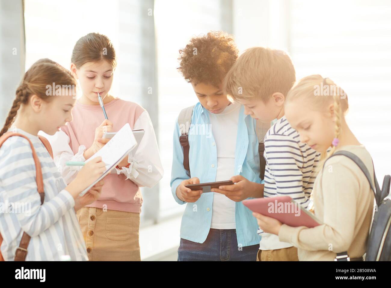 Gruppo di cinque studenti pensivi che si trovano insieme nel corridoio scolastico a discutere il loro progetto, colpo orizzontale Foto Stock