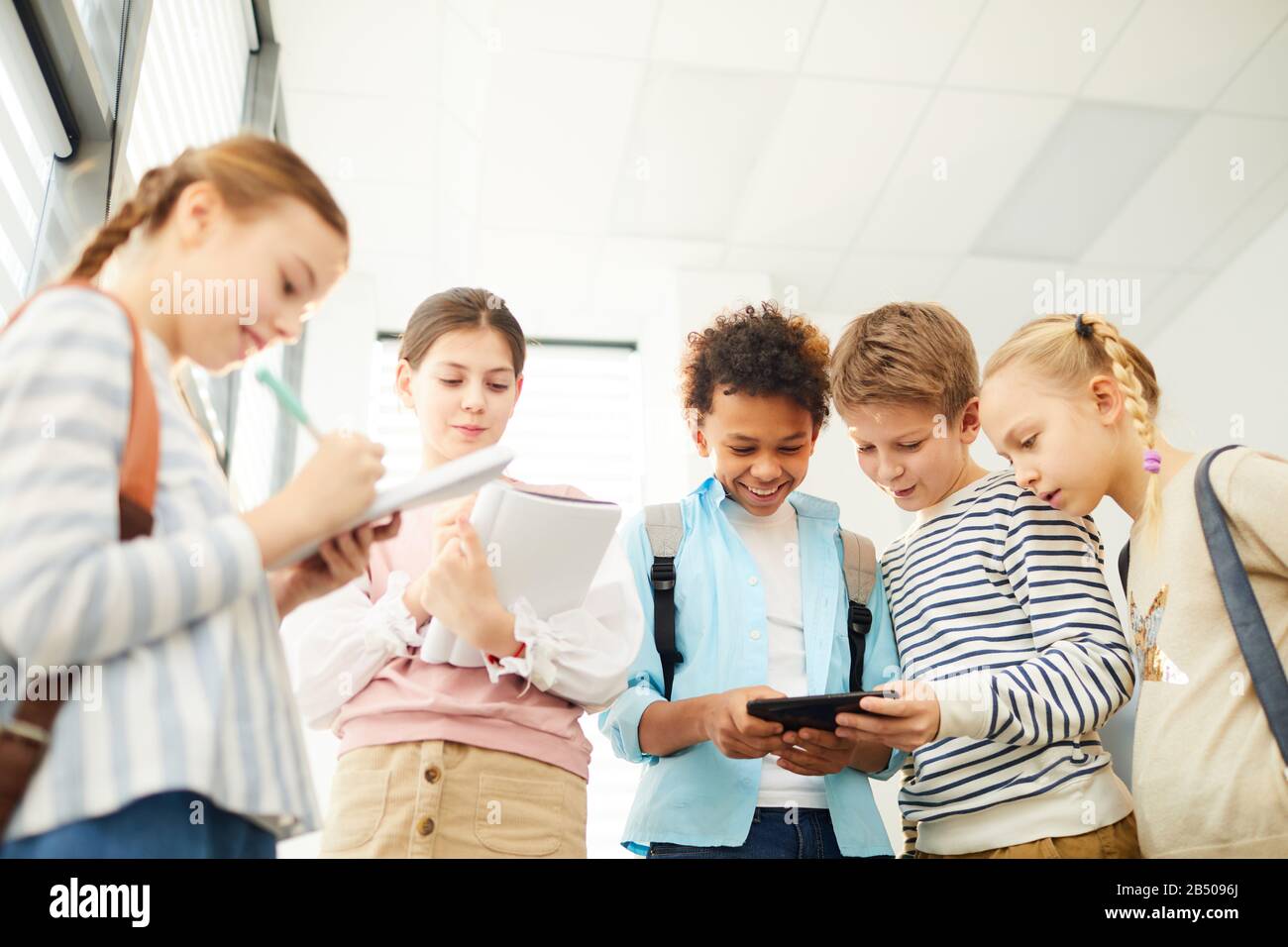 Allegri ragazzi e ragazze che si divertono a stare insieme nel corridoio della scuola guardando qualcosa in Internet e chiacchierando Foto Stock