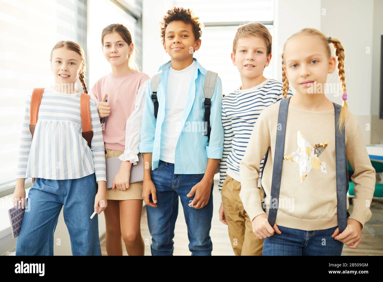 Ritratto di due ragazzi e tre ragazze in piedi insieme nel corridoio della scuola in posa sulla macchina fotografica, orizzontale medio lungo scatto Foto Stock
