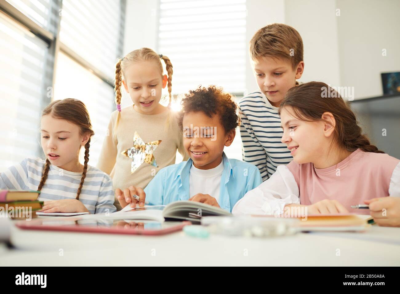 Gruppo di curiosi studenti medi che trascorrono il tempo di pausa insieme in classe guardando attraverso illustrazioni libro, scatto orizzontale Foto Stock