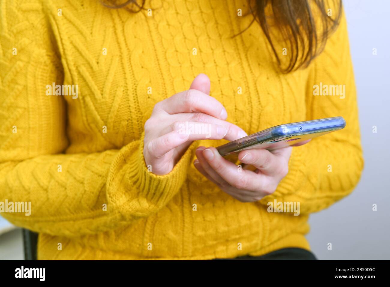 Smartphone nelle mani di una donna in un maglione giallo caldo, un concetto sul tema della datazione sui social network, shopping su Internet Foto Stock
