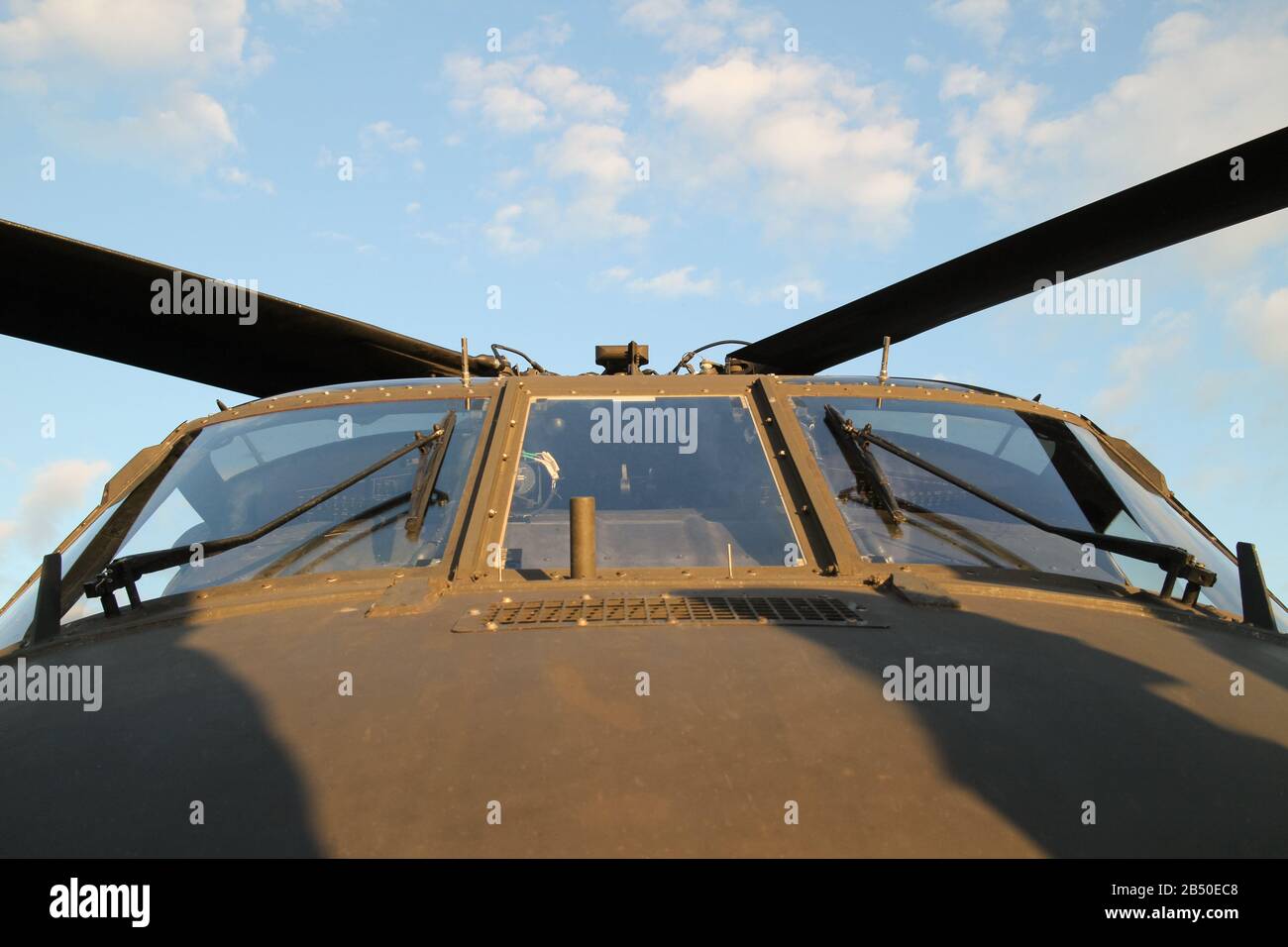 primo piano vista dal basso di un cockpit parabrezza di un elicottero militare olivo drab contro un cielo blu Foto Stock