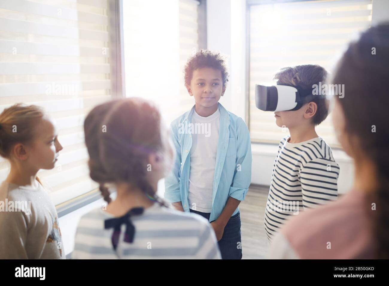 Studenti della scuola media che testano occhiali VR, i suoi compagni di classe che si stanno intorno a lui aspettando il loro turno Foto Stock