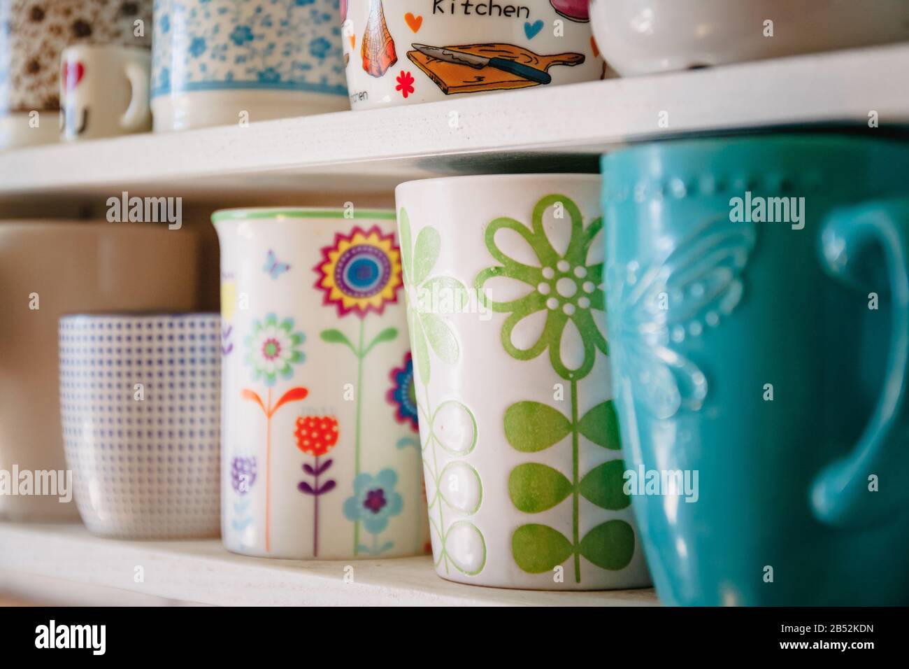 Una varietà di tazze e tazze in ceramica in primavera floreale luminoso stile stand in una fila su uno scaffale bianco casa. Foto Stock