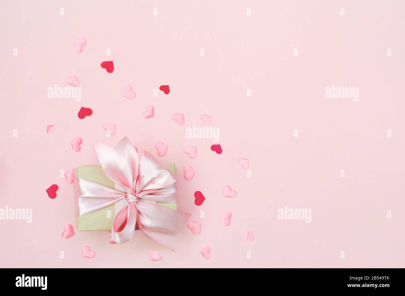 Presente con arco rosso su sfondo rosa con luccichio. Stile alla moda a disposizione piatta. Foto Stock
