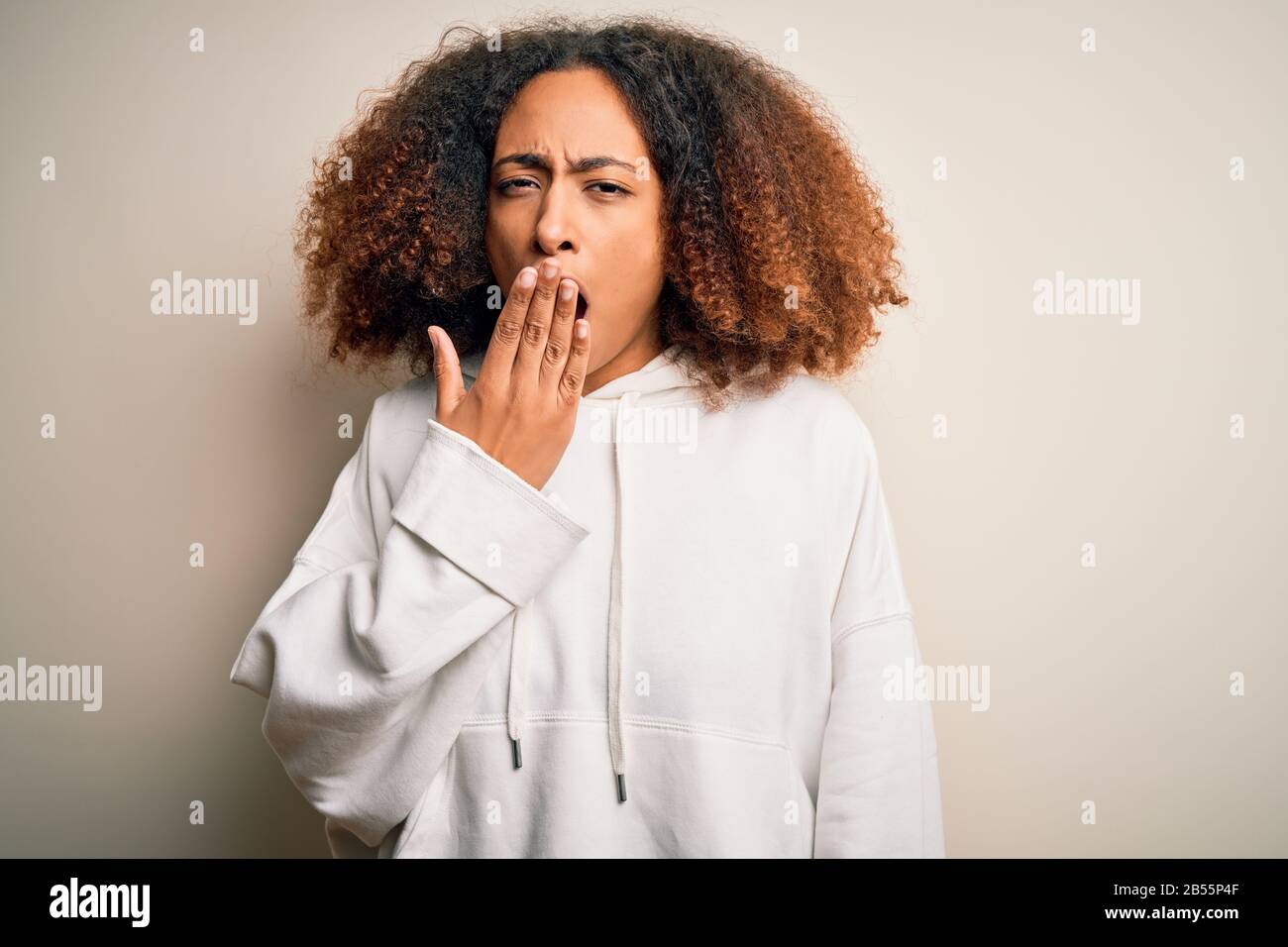 Giovane sportswoman afroamericano con capelli afro indossando felpa sportiva annoiata tenda stanco che copre la bocca con la mano. Irrequietezza e sonnolenza. Foto Stock